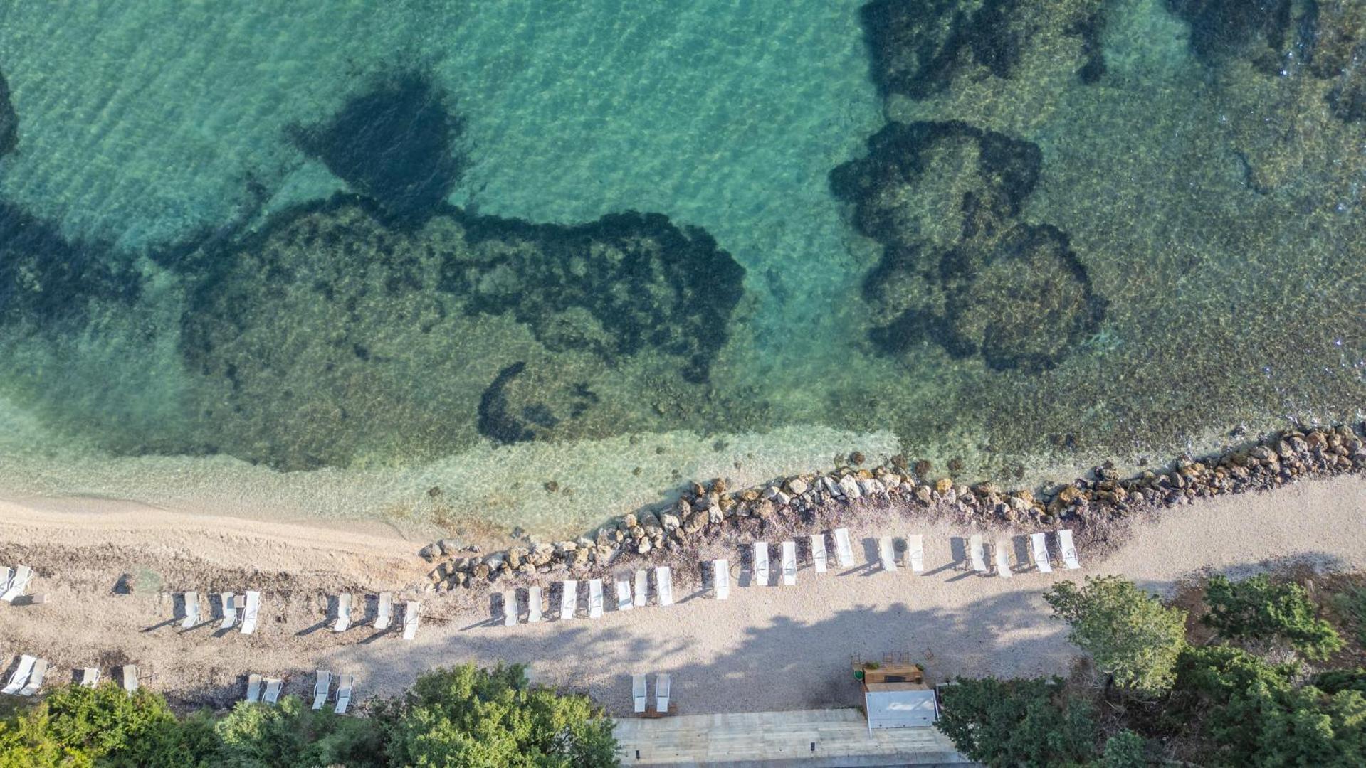 Mythos Palace Resort privātā pludmale no putna lidojuma ar dzidru ūdeni, akmeņainu gultni un sauļošanās krēsliem