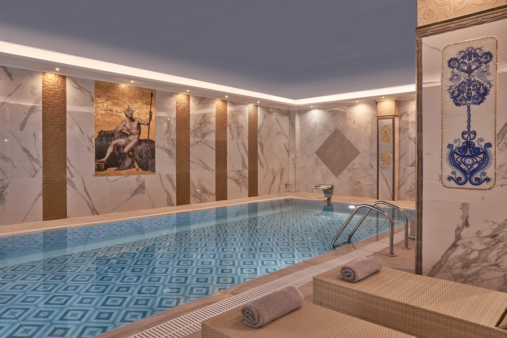 Mythos Palace Resort iekštelpu baseins ar mozaīkas sienas dekoru un atpūtas krēsliem spa centrā Georgiupoli, Krētā
