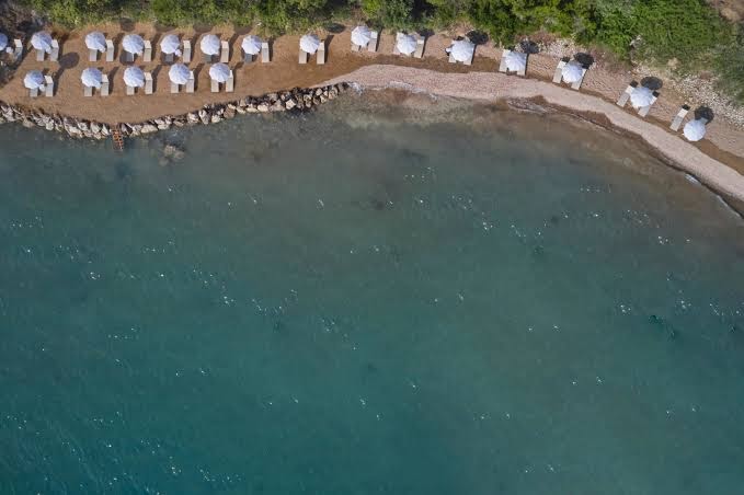Mythos Palace Resort pludmales zona no augšas ar baltiem saulessargiem un gultām smilšainā piekrastē pie jūras