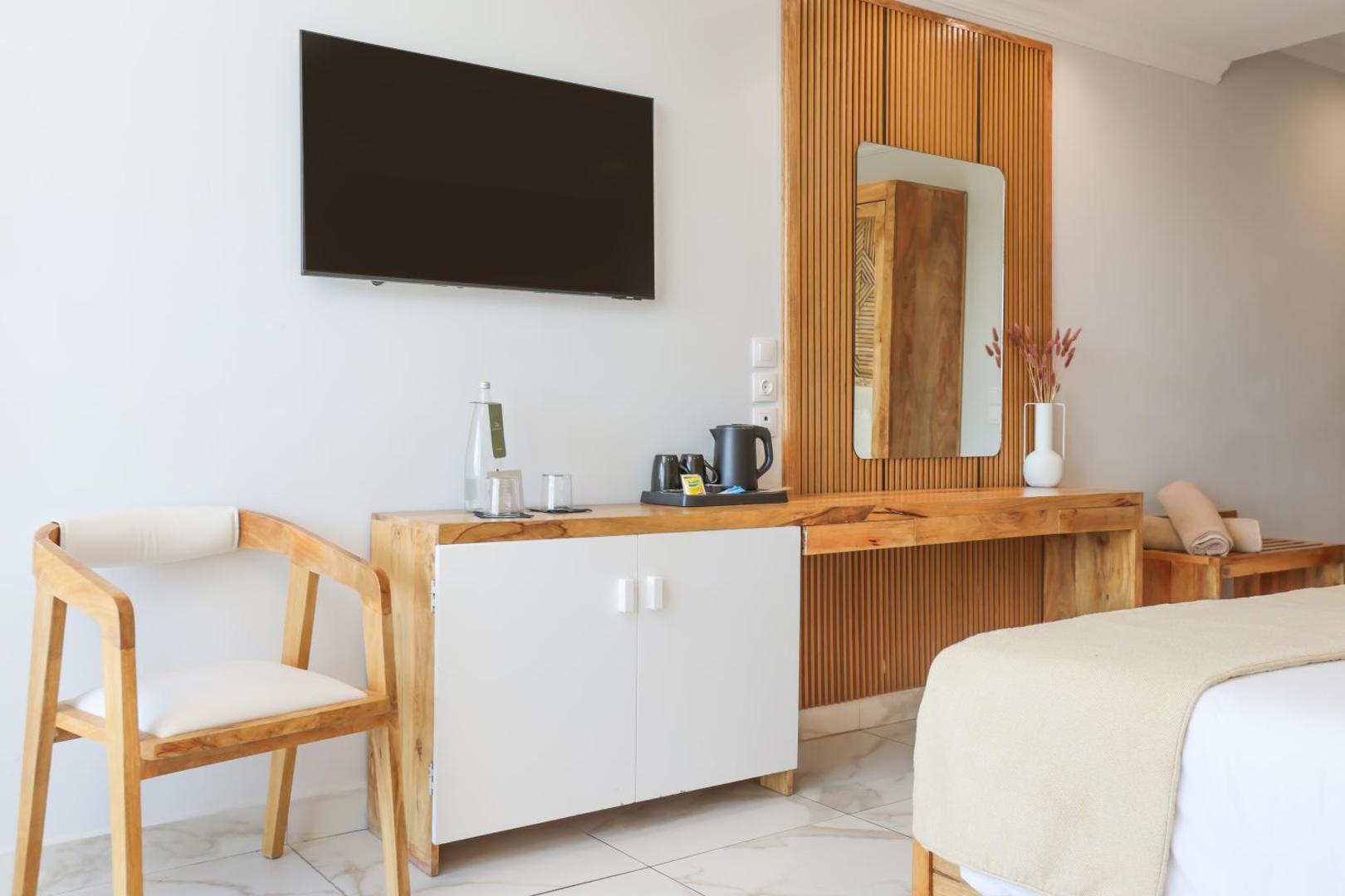 Gaišs Mythos Palace Resort numura interjers ar darba galdu, TV un koka krēslu Korfu piekrastē