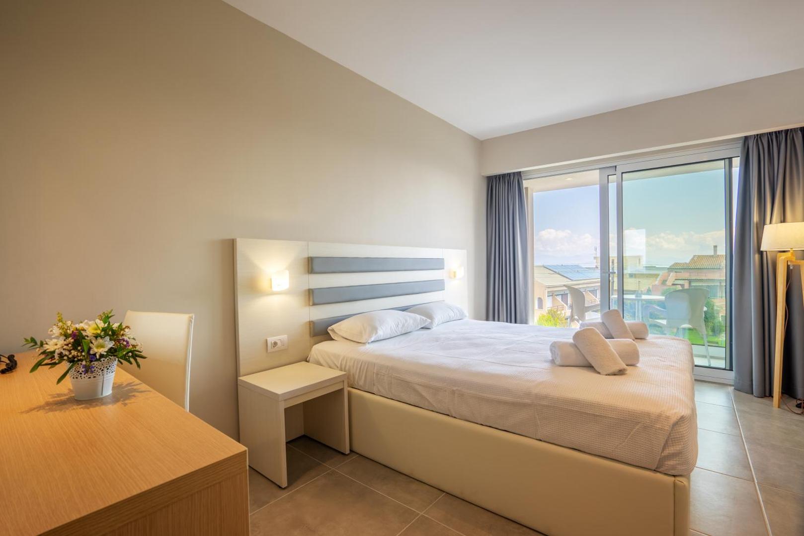 CNic Gemini Hotel gaišs divvietīgs numurs ar balkonu Mesongi kūrortā Korfu — liela gulta, rakstāmgalds un skats uz apkārtni