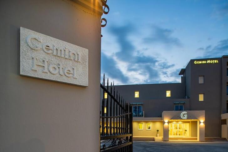 CNic Gemini Hotel nosaukuma plāksne pie vārtiem un izgaismota galvenā ēka krēslas stundā Mesongi, Korfu