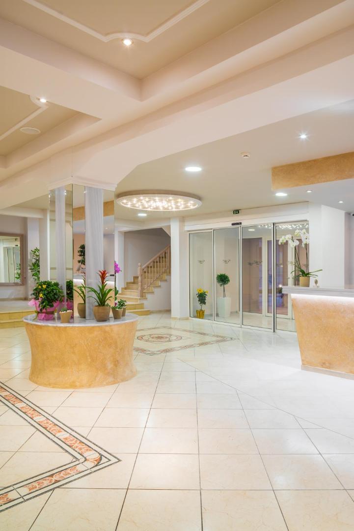 CNic Gemini Hotel gaišais vestibils ar recepcijas leti, flīžu grīdu un dekoratīviem augiem Mesongi ciemā Korfu