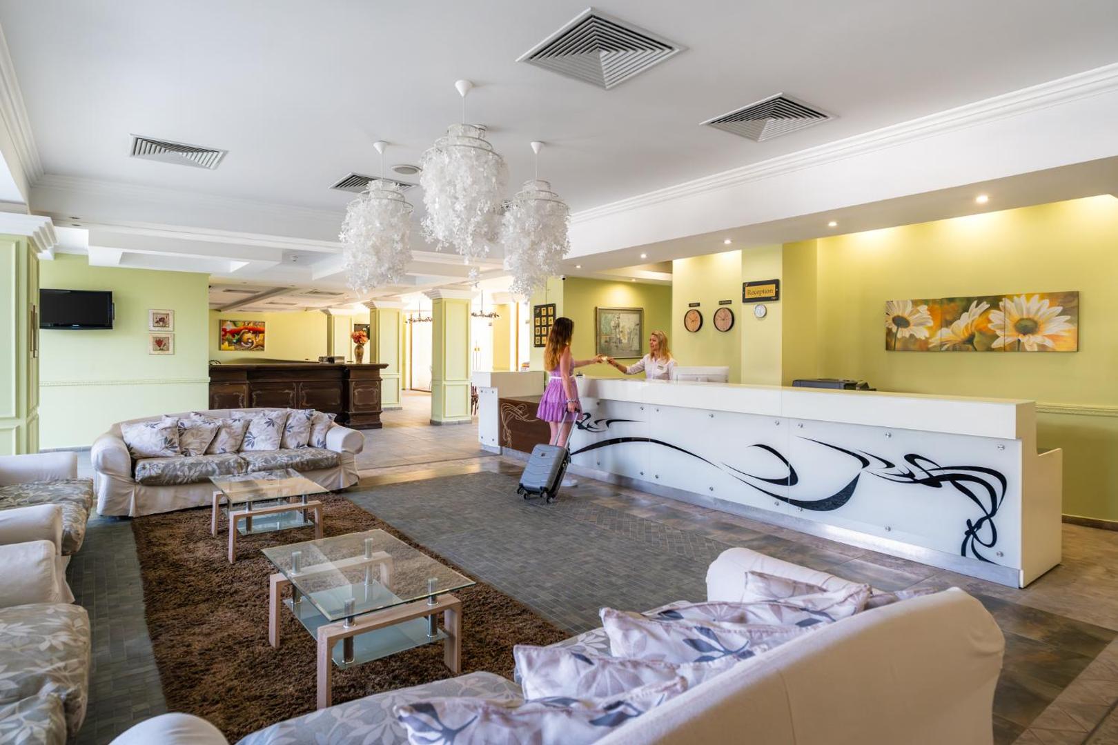 Festa Pomorie Resort viesnīcas vestibils un recepcijas zona ar gaišiem dīvāniem, stikla galdiņiem un dekoratīvām lustrām Pomorijā