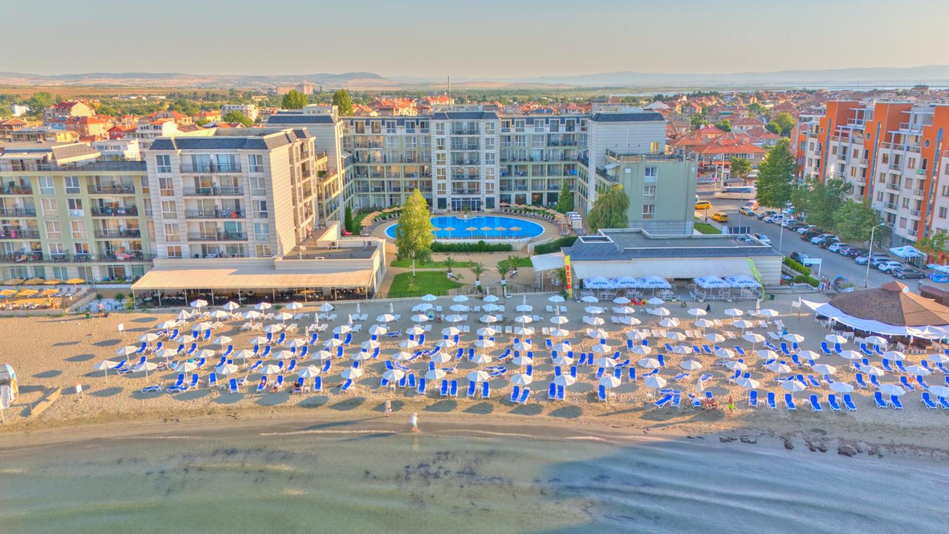 Festa Pomorie Resort pludmales zona ar daudziem saulessargiem un sauļošanās krēsliem, fonā redzams āra baseins un viesnīcas fasāde