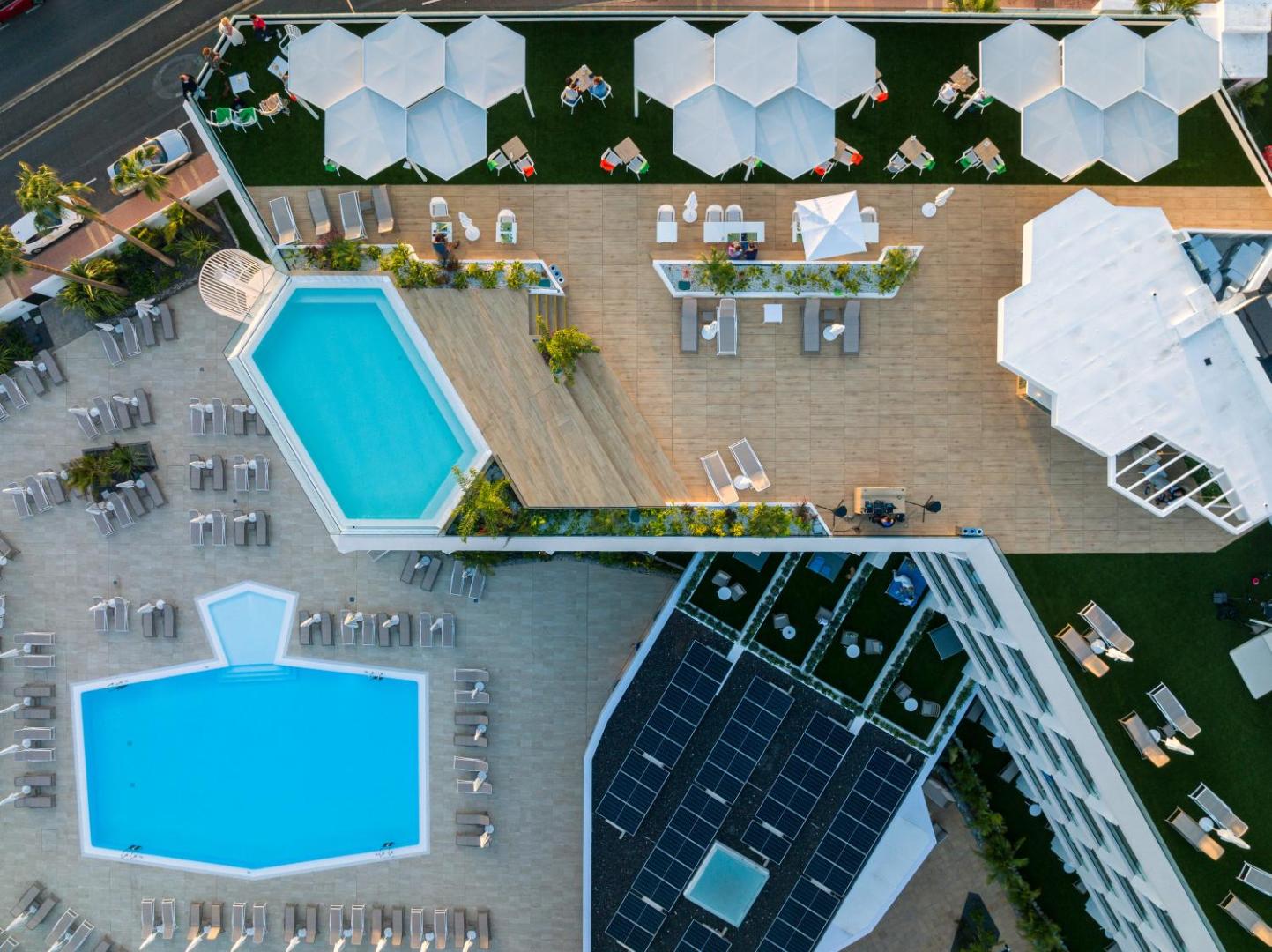 Viesnīcas MYND Adeje skats no putna lidojuma uz diviem āra baseiniem un jumta terasi ar atpūtas zonu Tenerifē
