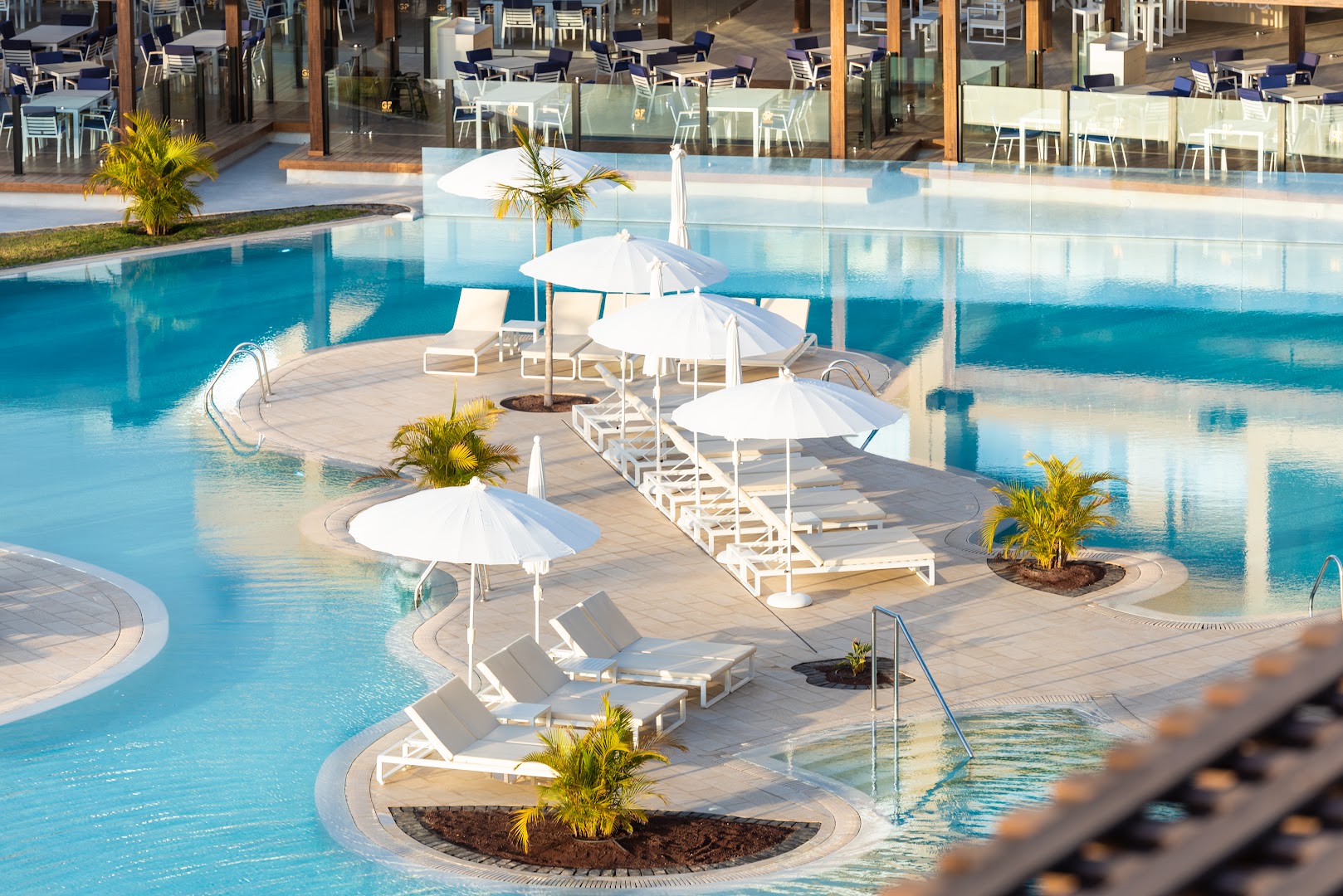 GF Victoria viesnīcas plašais āra baseins ar atpūtas zonu uz salas, saulessargiem un zviļņiem Tenerifē, Kanāriju salās.