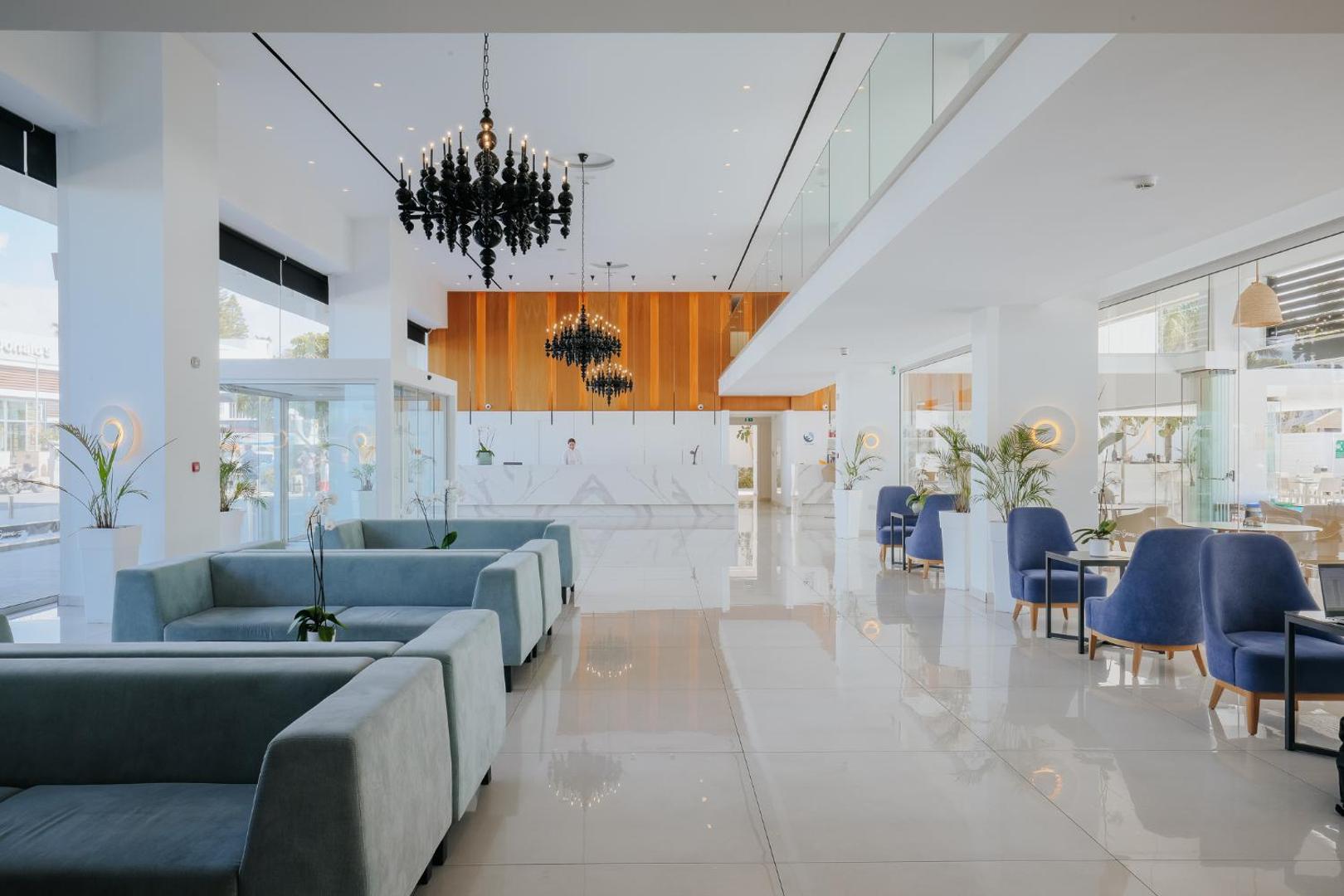 Tasia Maris Seasons Hotel gaišais vestibils ar modernām mēbelēm, zilām atpūtas krēsliem, melnām lustrām un marmora recepcijas leti
