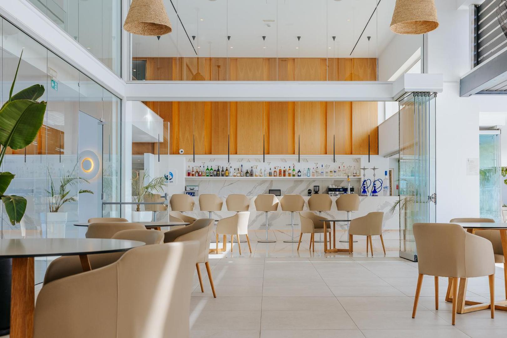 Tasia Maris Seasons Hotel gaišais bārs ar augstajiem krēsliem, koka paneļiem un plašu dzērienu izvēli pie marmora letes