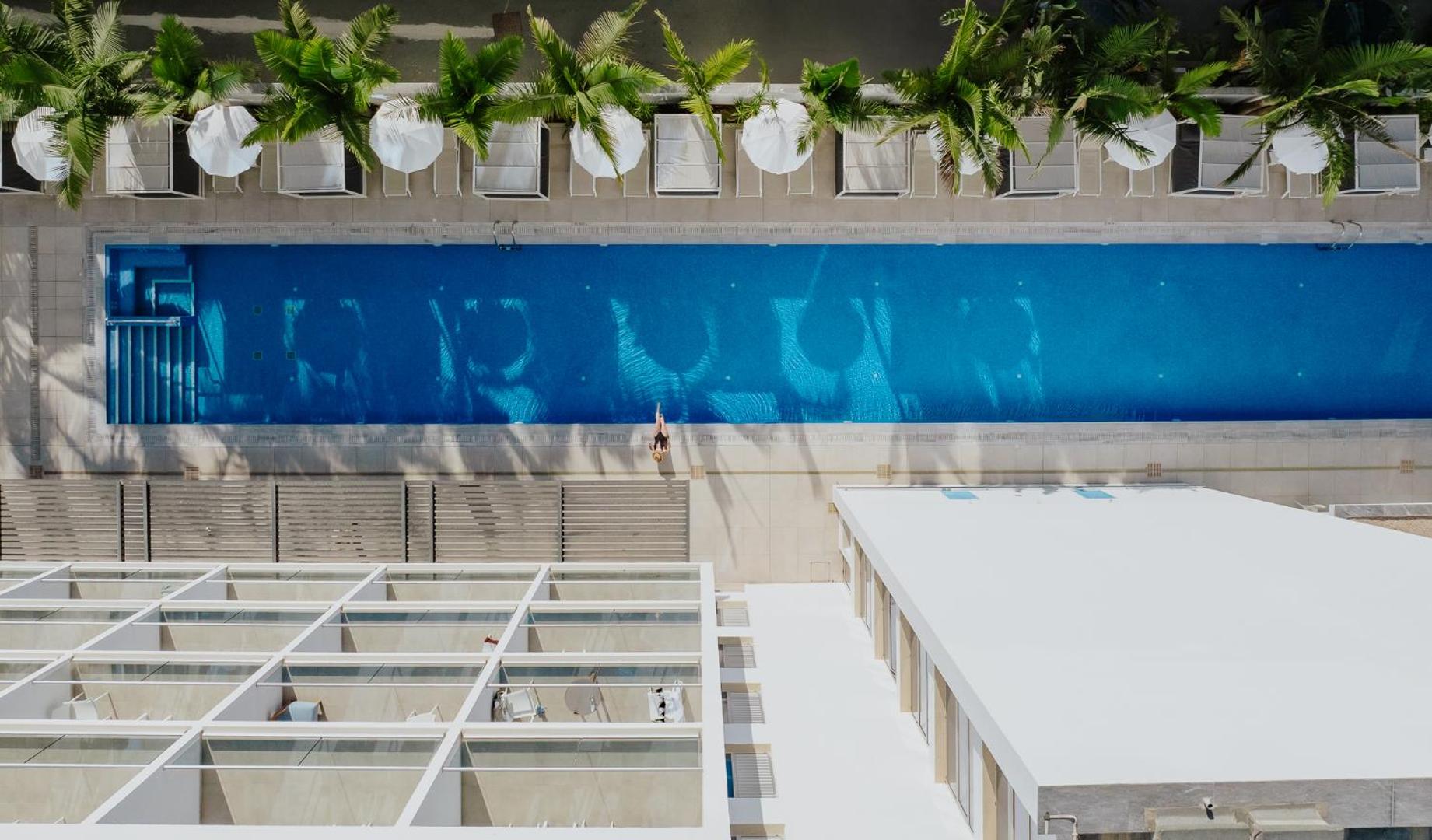 Tasia Maris Seasons Hotel skats no augšas uz garo peldbaseinu un sauļošanās zonu ar baltiem saulessargiem un palmām Ajanapā