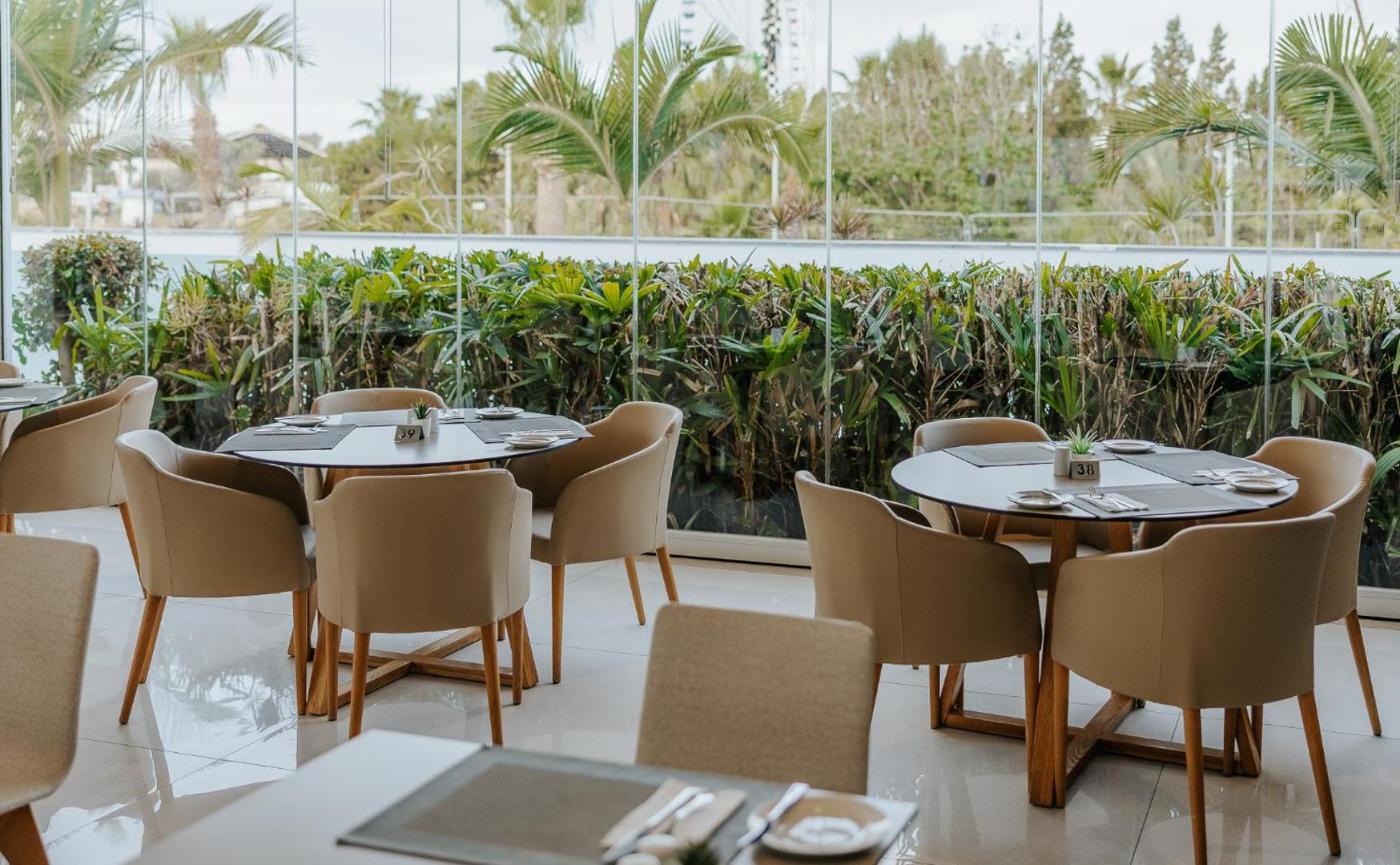 Tasia Maris Seasons Hotel modernā restorāna interjers ar gaišām mēbelēm un lieliem logiem uz dārzu Ajanapā