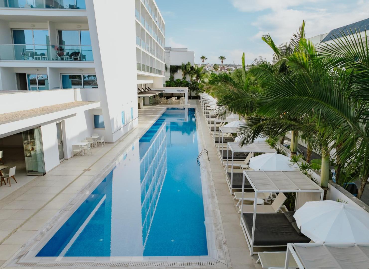 Tasia Maris Seasons Hotel garais āra baseins ar modernām atpūtas nojumēm un palmām Aijanapas kūrortā, Kiprā.