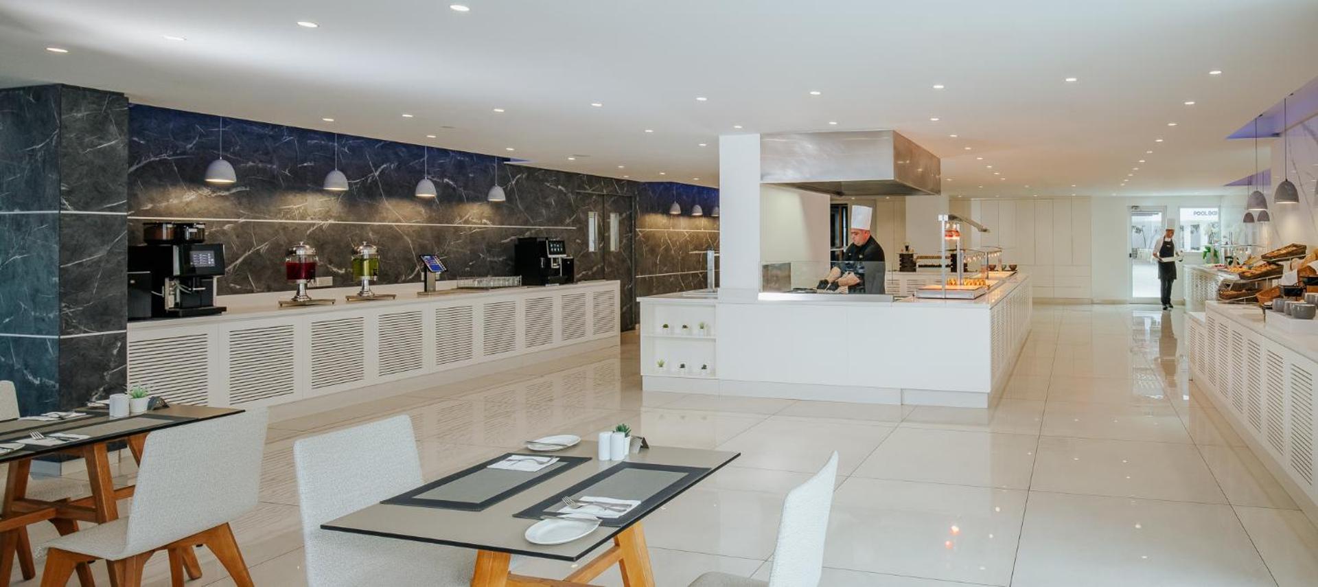 Tasia Maris Seasons Hotel restorāna bufetes zona ar marmora sienām, kafijas automātiem un pavāru pie atvērtās virtuves letes