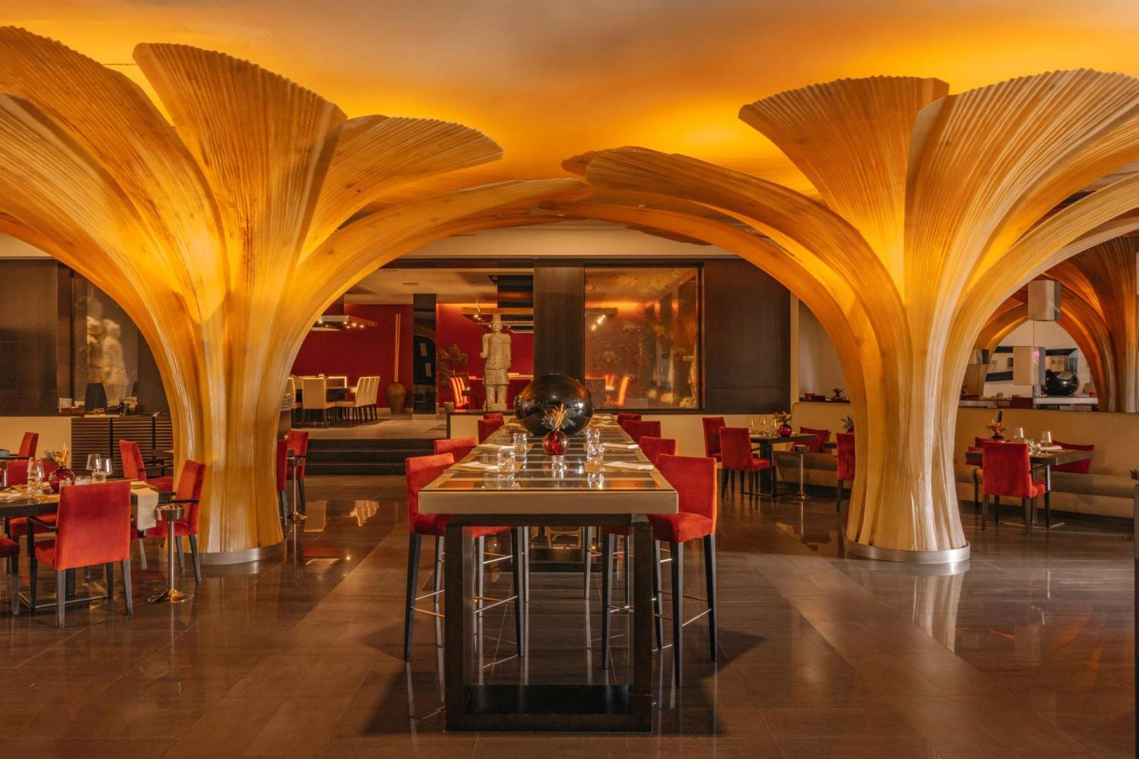 Gran Melia Palacio de Isora tematiskais restorāns ar unikālām koka kolonnu instalācijām, sarkanām mēbelēm un siltu apgaismojumu Tenerifē.