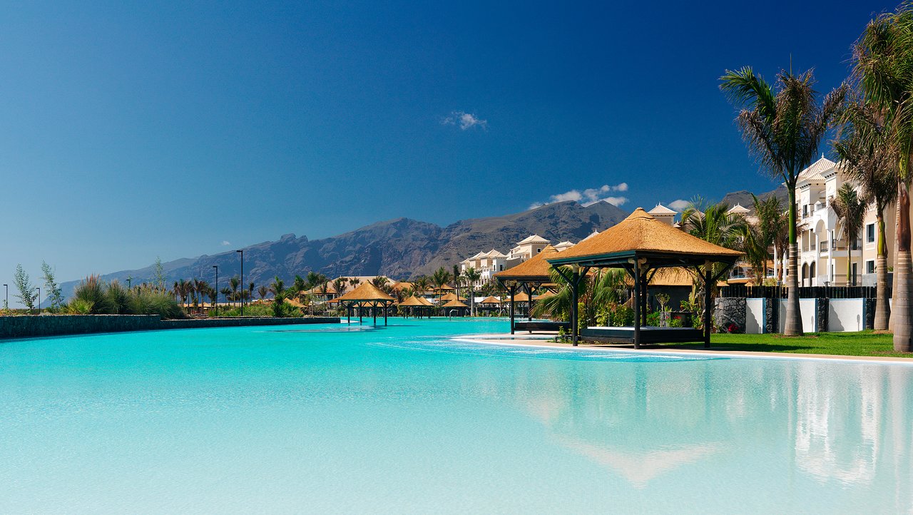 Gran Melia Palacio de Isora milzīgs sālsūdens baseins ar atpūtas nojumēm un skatu uz kalniem Tenerifes piekrastē