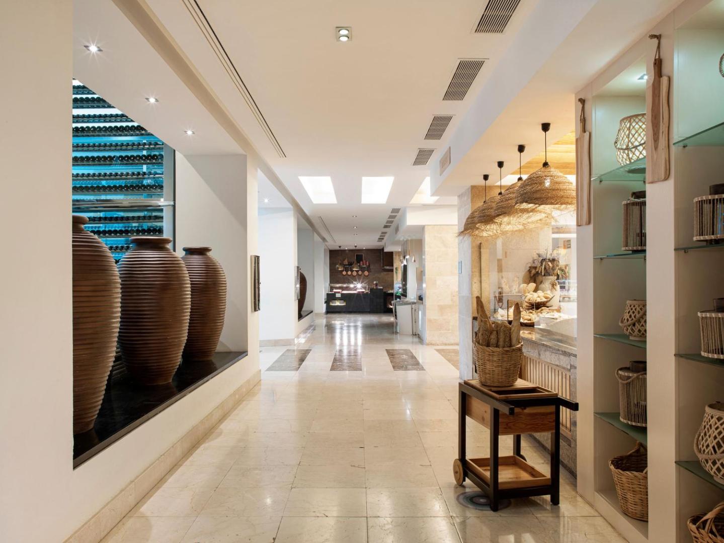 Gran Melia Palacio de Isora viesnīcas restorāna interjers Tenerifē ar māla vāzēm, dekoratīviem groziem un maizes bufetes zonu gaišā gaitenī