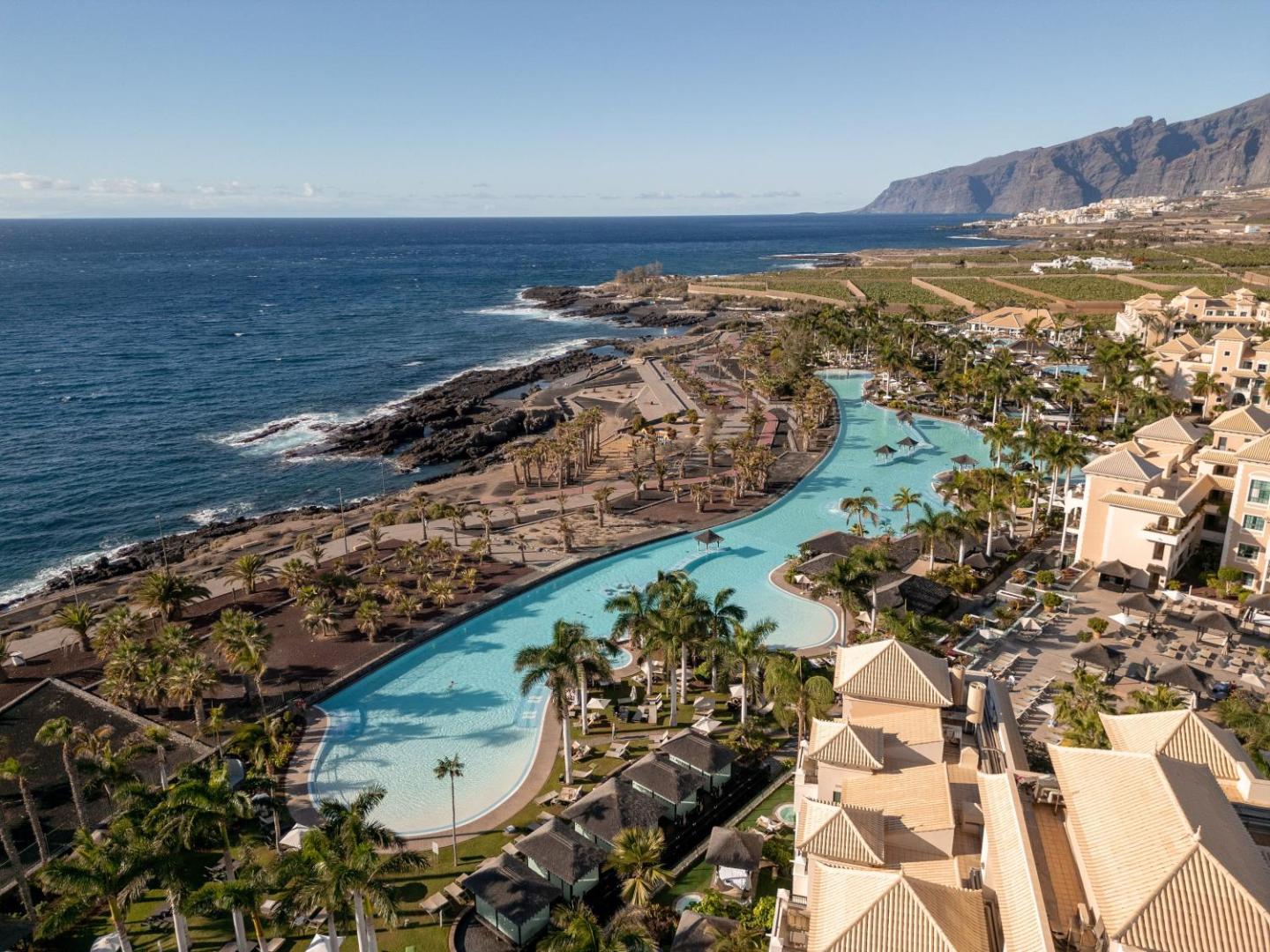 Gran Melia Palacio de Isora panorāmas skats uz plašo baseinu kompleksu un okeāna piekrasti Tenerifē ar kalniem fonā