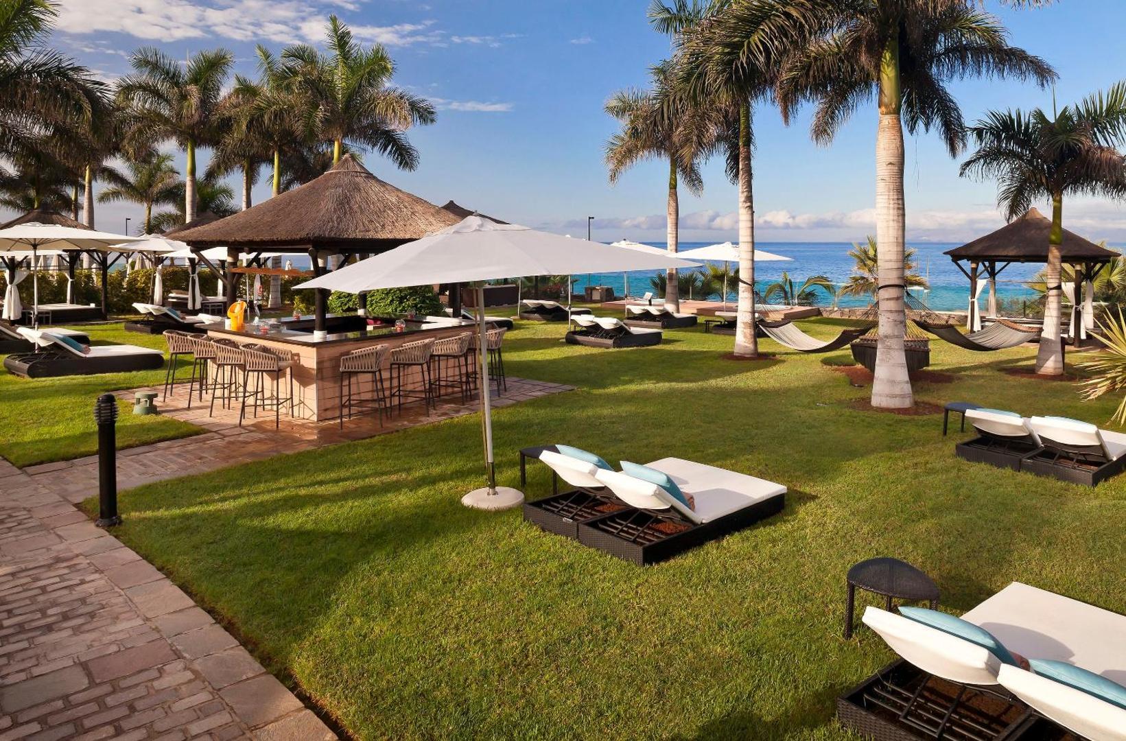 Gran Melia Palacio de Isora āra bārs un atpūtas zona zālienā ar sauļošanās krēsliem, saulessargiem un skatu uz okeānu