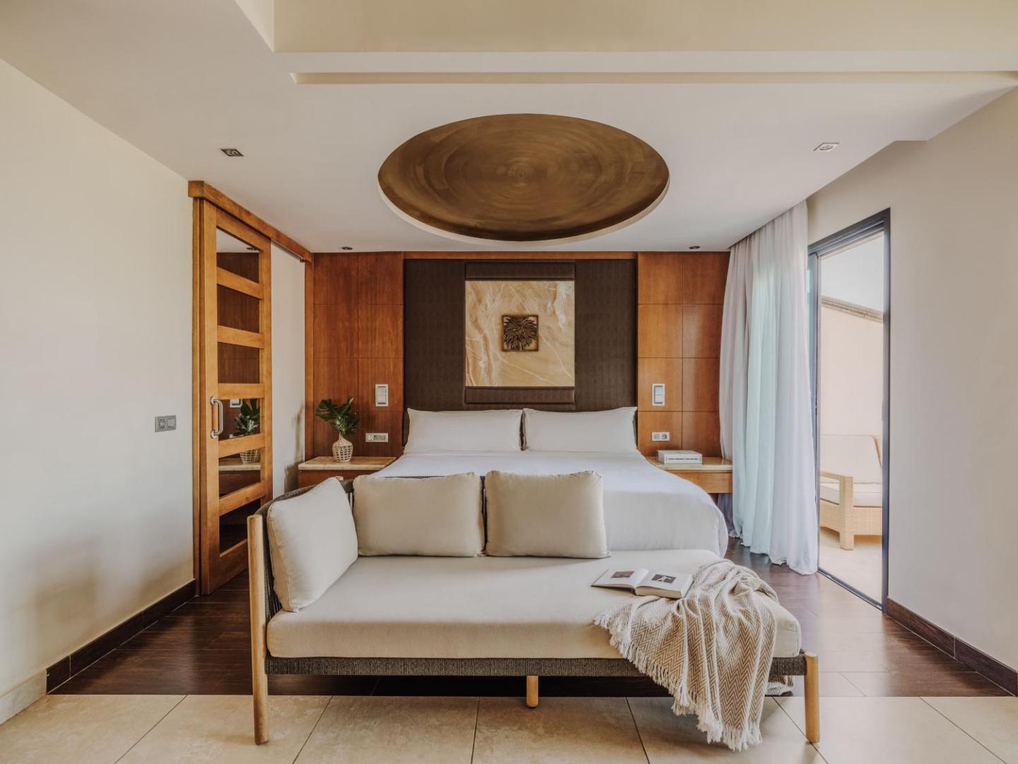 Gran Melia Palacio de Isora luksusa numura interjers ar plašu gultu, dīvānu un koka apdari kūrortā Tenerifē