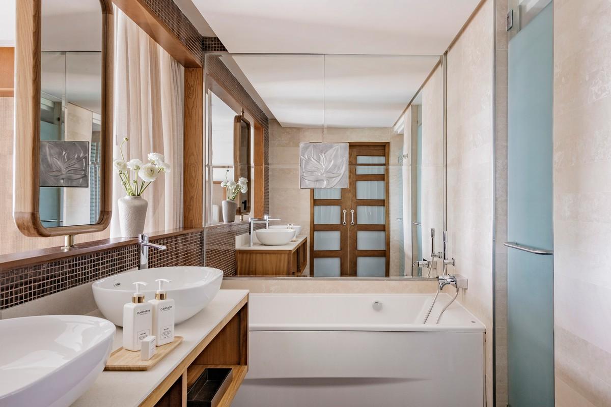 Gran Melia Palacio de Isora moderns vannas istabas numurs ar baltu vannu, divām izlietnēm, lielu spoguli un koka apdares elementiem.