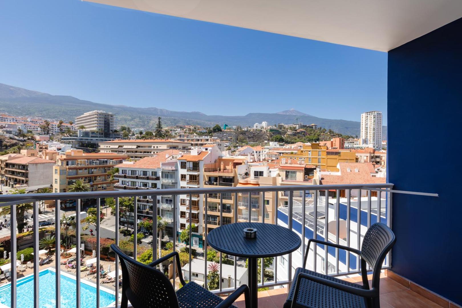 Skats no Catalonia Las Vegas viesnīcas balkona uz Puerto de la Cruz pilsētu, kalniem un āra baseinu Tenerifē