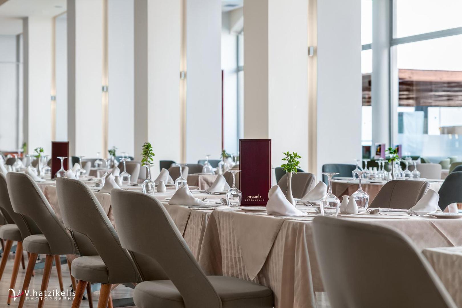 Kresten Palace Hotel Olympia restorāna interjers ar gariem, balti klātiem galdiem un modernu dizainu Rodas salā