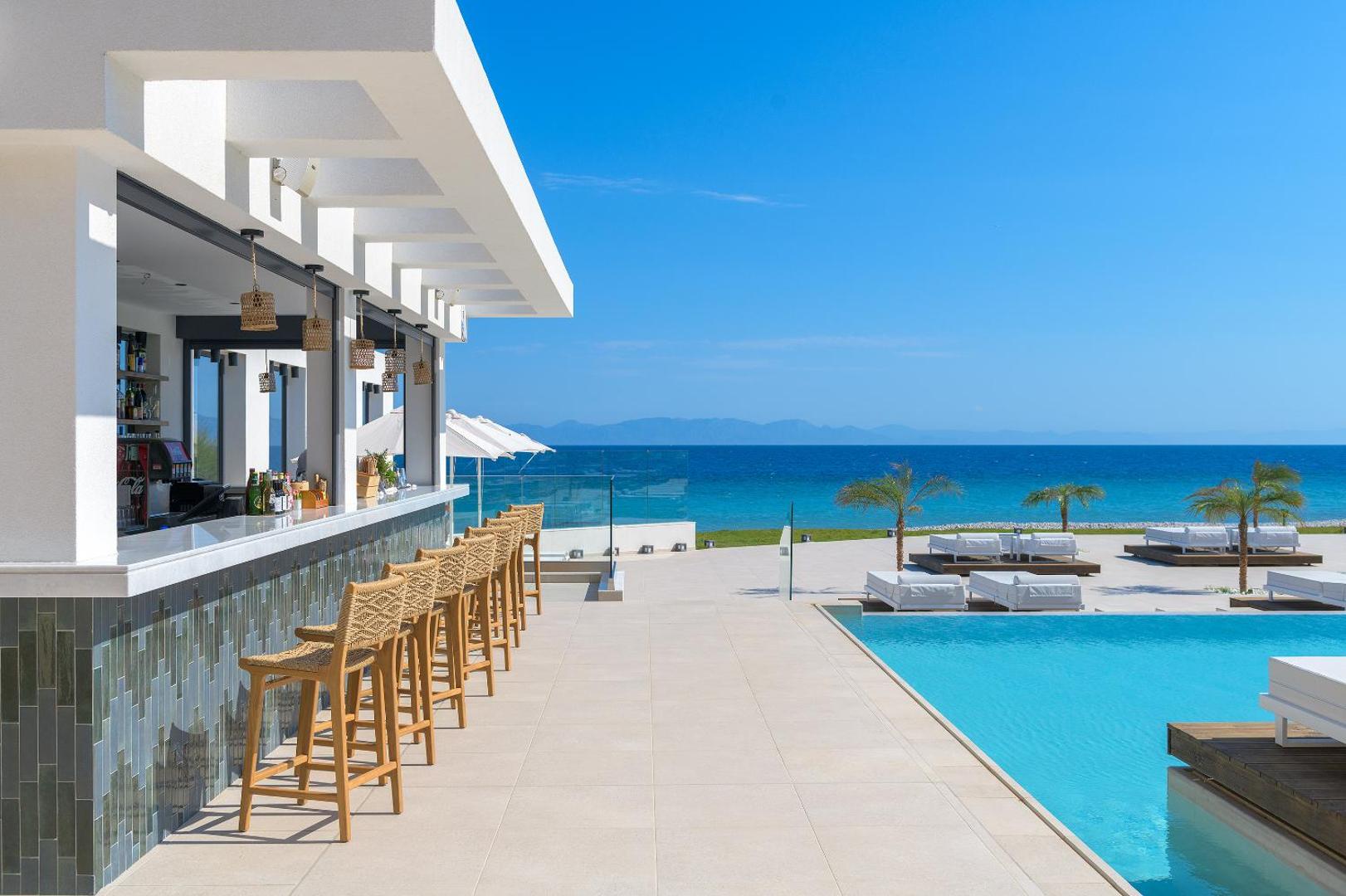 Sun Beach Resort pludmales bārs pie baseina Rodā — bāra lete ar augstiem krēsliem, skats uz zilo jūru un atpūtas zonu.