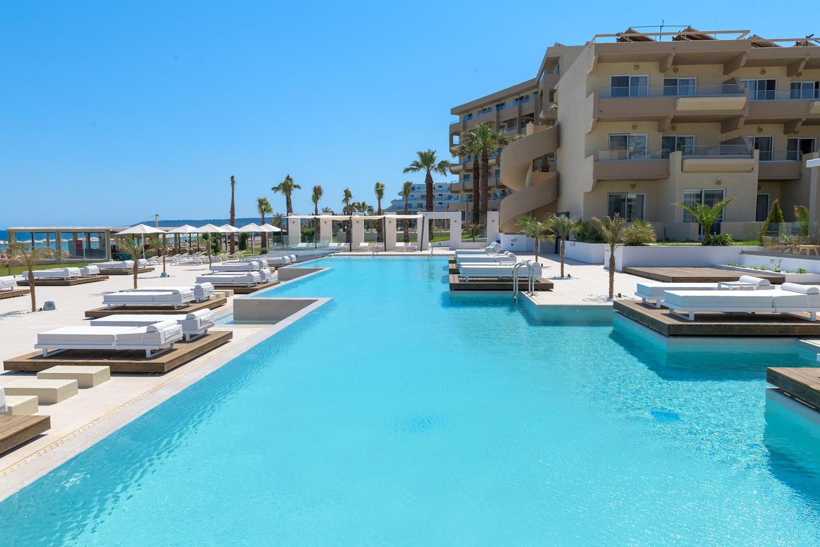 Sun Beach Resort galvenais āra baseins ar sauļošanās krēsliem uz koka platformām Rodas salā, Grieķijā, blakus viesnīcas korpusam