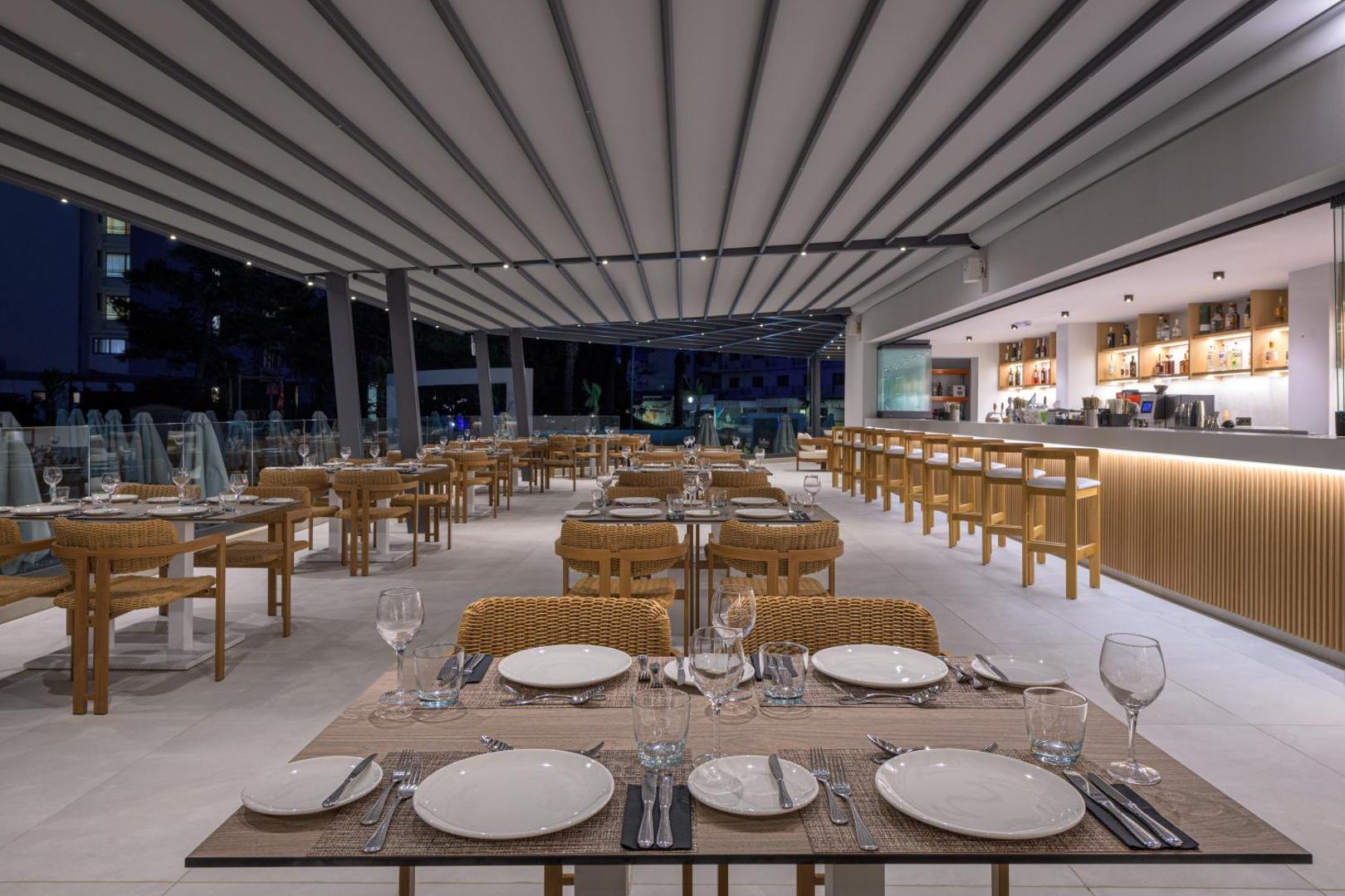 Sun Beach Resort vakara bārs un restorāna zona ar siltu apgaismojumu, pītiem krēsliem un servētiem galdiem Rodas kūrortā.