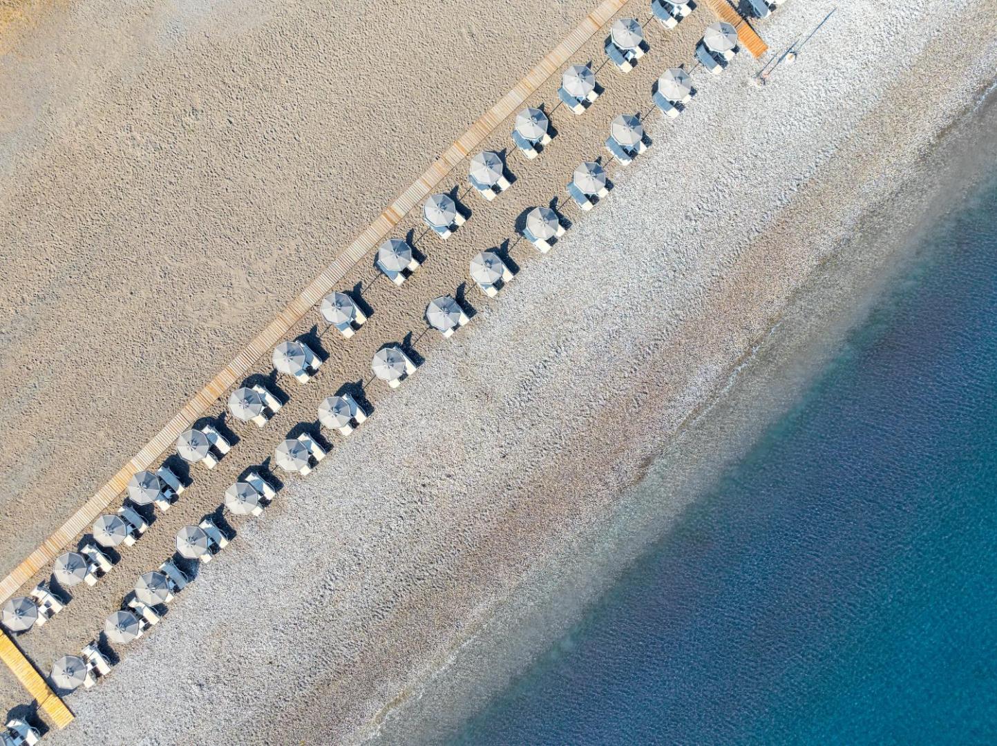 Aerofoto uzņēmums ar Sun Beach Resort pludmales saulessargiem un koka laipām Rodas piekrastē — zila jūra un gaišas smiltis