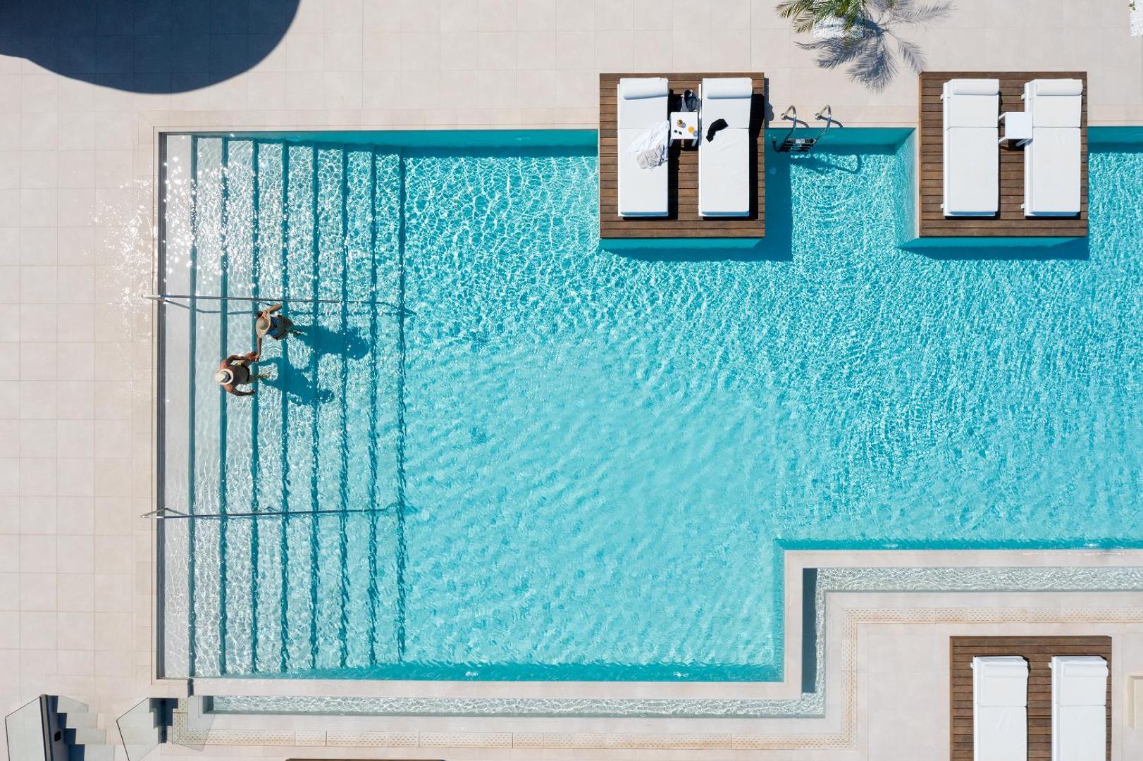 Skats no augšas uz Sun Beach Resort baseinu ar pakāpieniem un sauļošanās platformām ūdenī, kur atpūšas viesi
