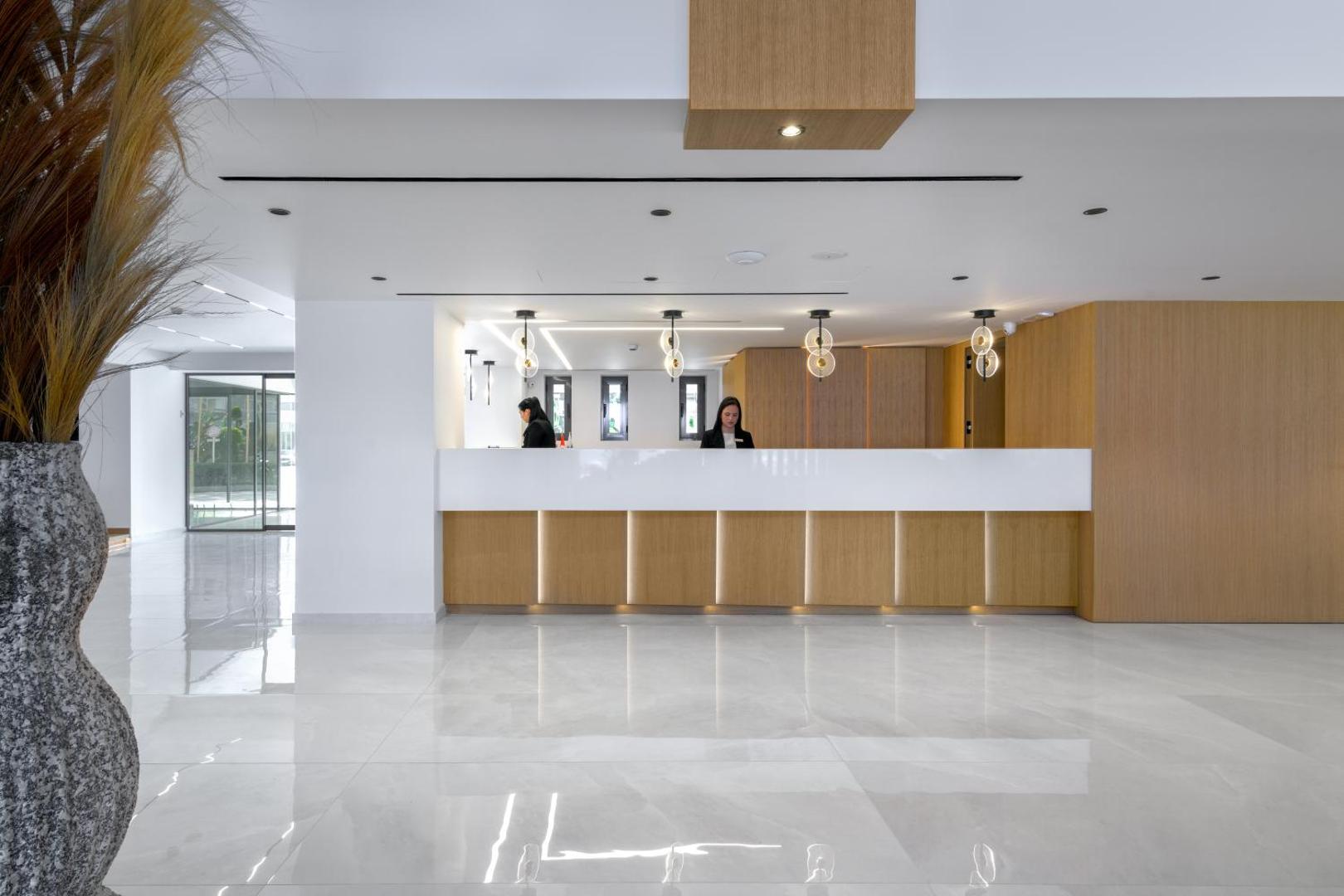 Sun Beach Resort modernā recepcijas zona Rodā, Grieķijā — gaišs vestibils ar koka apdari, minimālistisku dizainu un viesmīlīgu personālu pie reģistrācijas galdes.