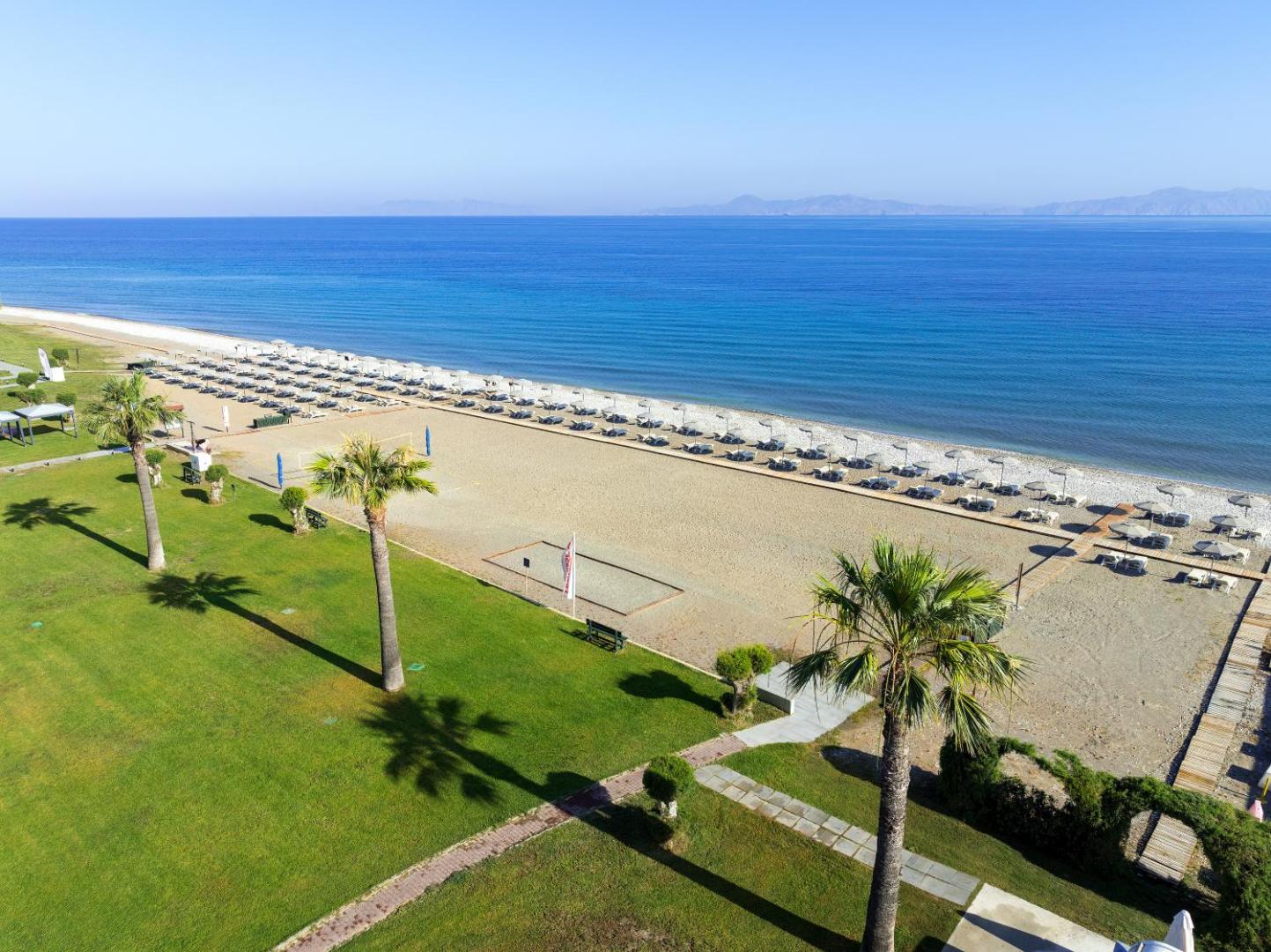 Sun Beach Resort apzaļumotā teritorija ar palmām un zālāju blakus pludmalei — skats uz jūru un atpūtas zonu Rodā