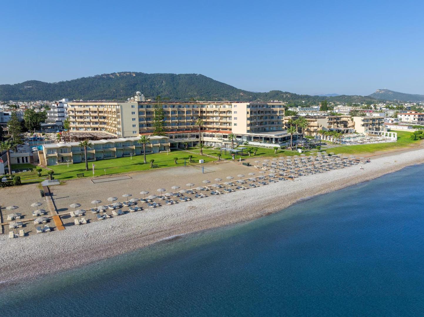Sun Beach Resort skats no jūras puses uz viesnīcas fasādi, zaļo zonu un saulessargiem pludmalē