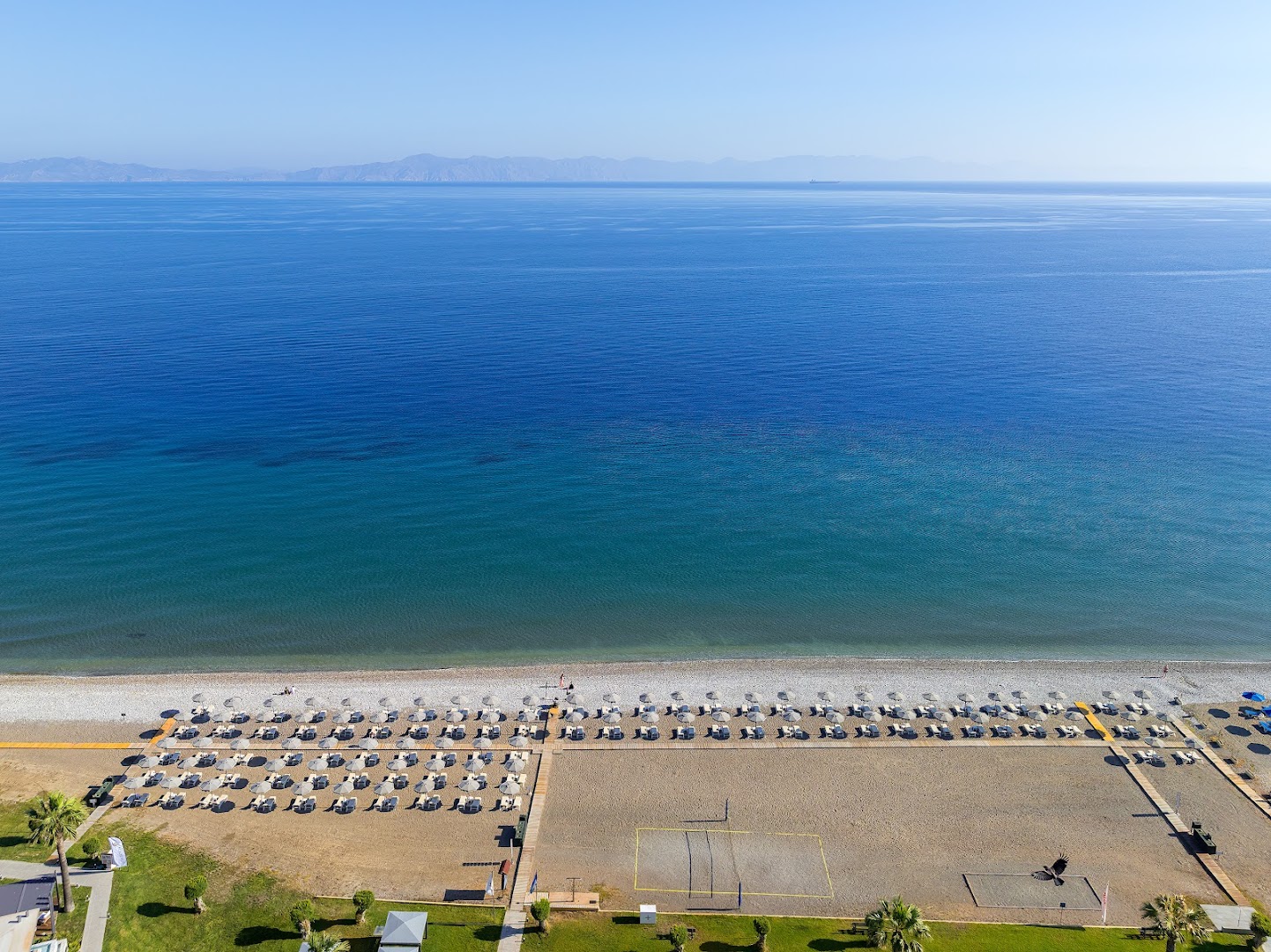 Sun Beach Resort plašā pludmale Rodas salā, Grieķijā — skats no augšas uz ziliem jūras ūdeņiem, saulessargiem un volejbola laukumu