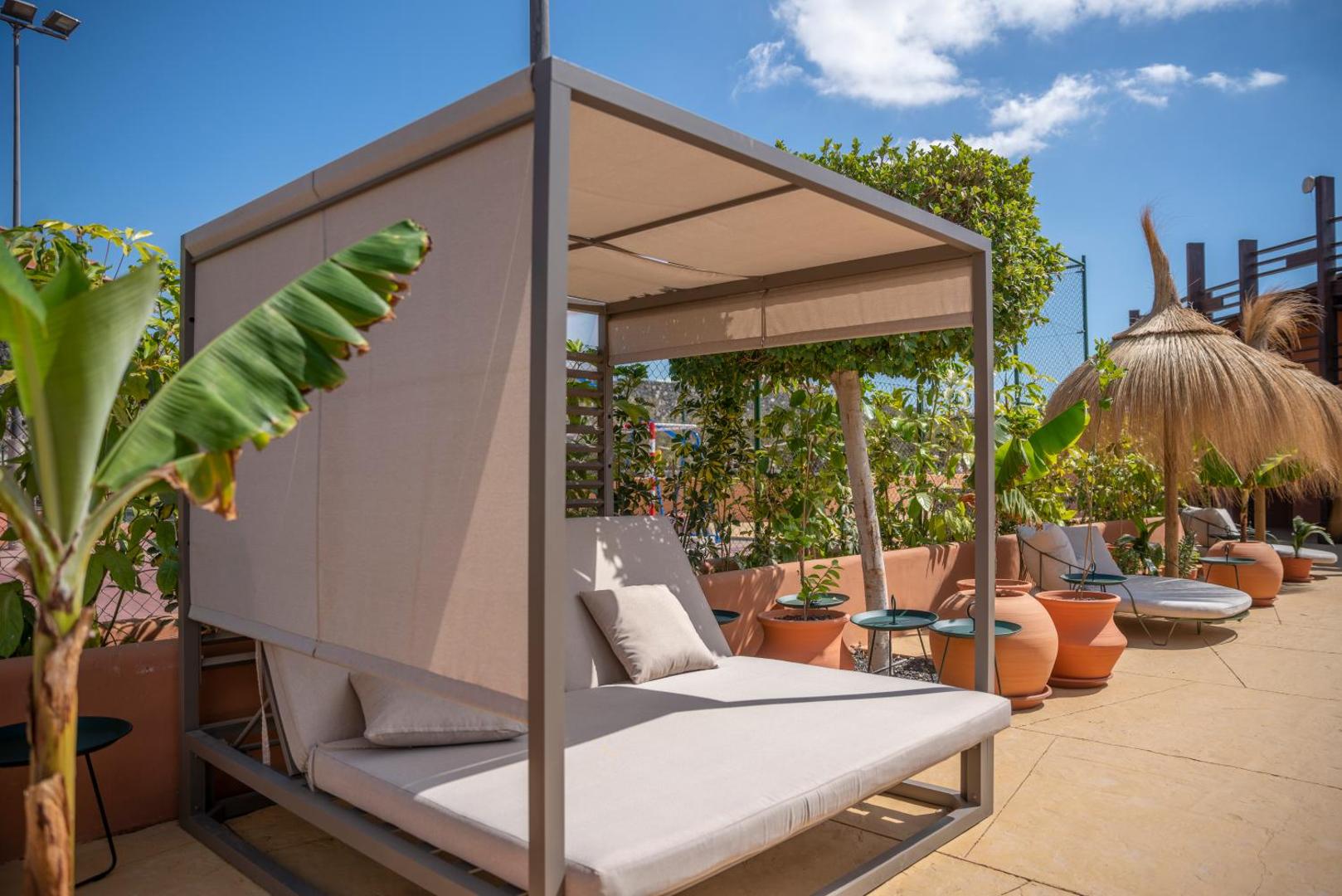 Barceló Tenerife Royal Level ekskluzīva atpūtas zona ar mīkstiem dienas sauļošanās krēsliem un nojumi dārza ielokā
