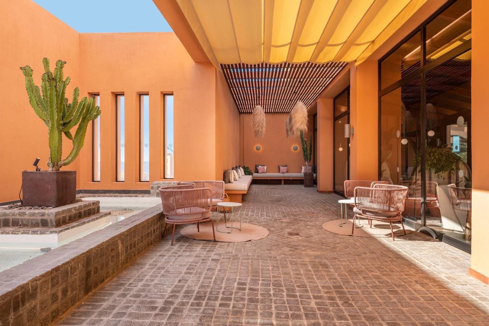 Barceló Tenerife Royal Level āra terase ar rozā atpūtas krēsliem, kaktusu un saules aizsegu siltos terakotas toņos