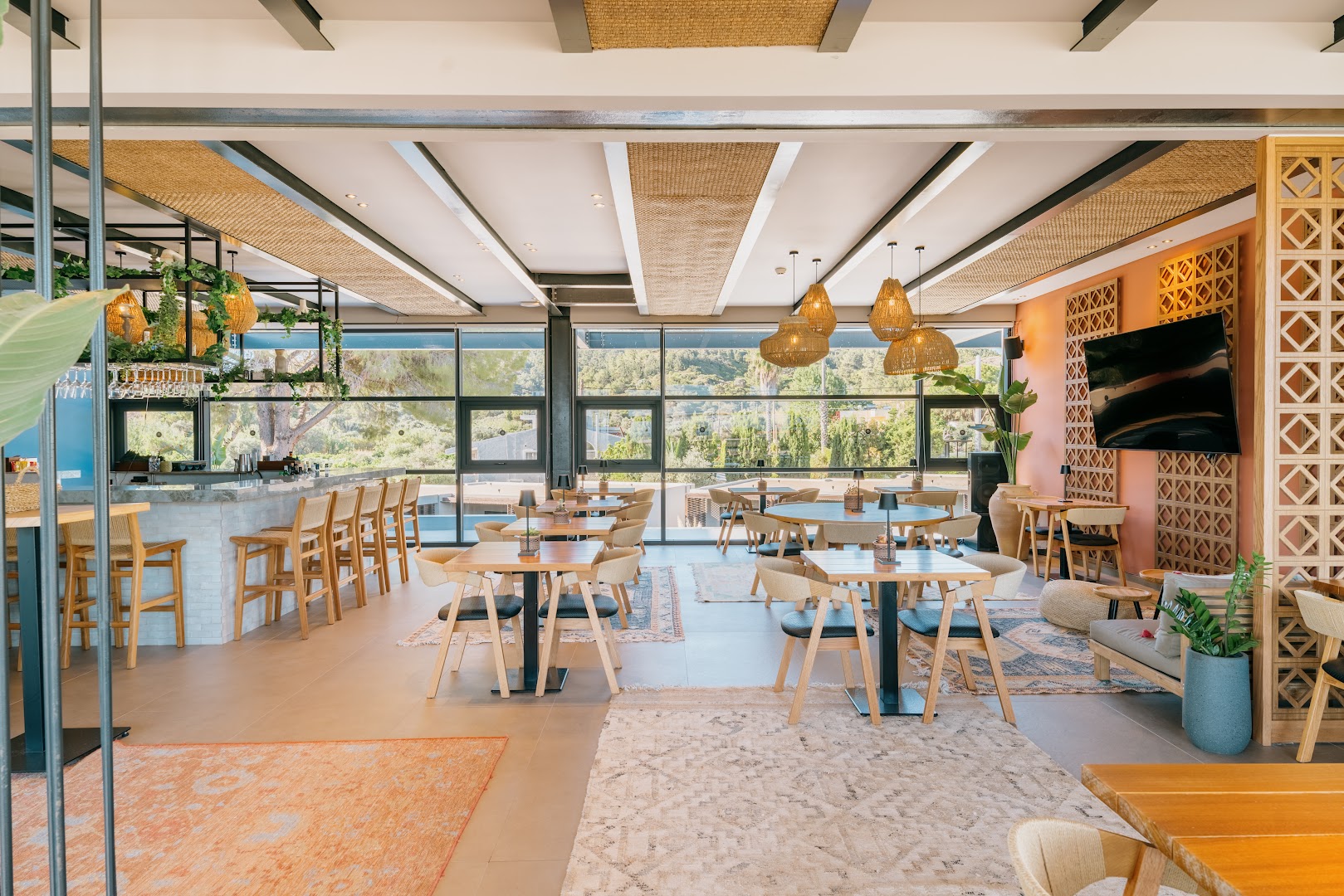 Cook's Club Ialysos Rhodes modernais iekštelpu bārs un atpūtas zona ar dizaina mēbelēm, paklājiem un lieliem logiem uz dārzu