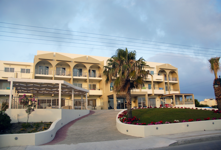 Sea Melody Beach Hotel Apartments fasāde un terases vakara gaismā Ialissos kūrortā — skats uz numuru balkoniem un dārzu