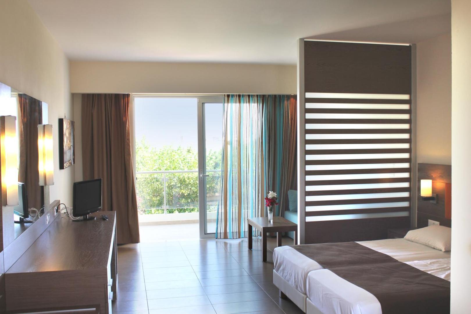 Sea Melody Beach Hotel Apartments gaišs viesnīcas numurs ar balkonu Rodas salā — mēbelēta atpūtas zona, divguļamā gulta un skats uz dārzu