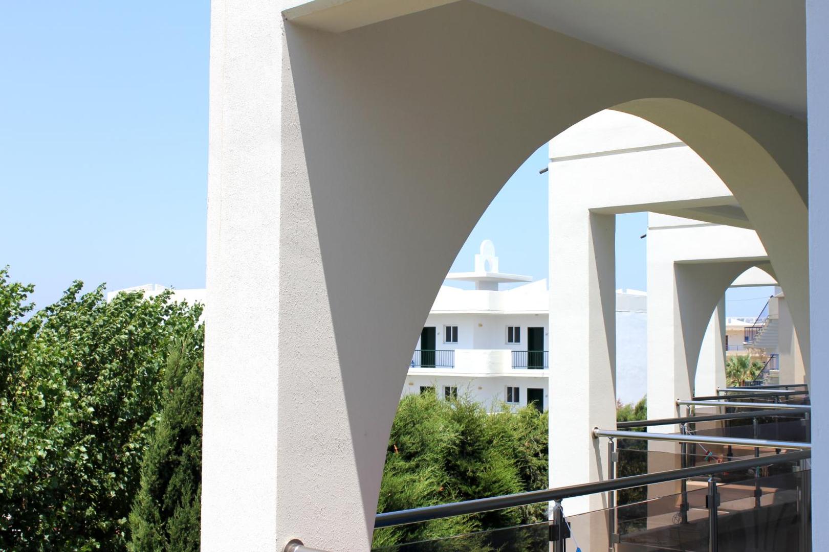 Skats no Sea Melody Beach Hotel Apartments numura balkona caur arkām — redzama kaimiņu ēka un zaļojoši koki