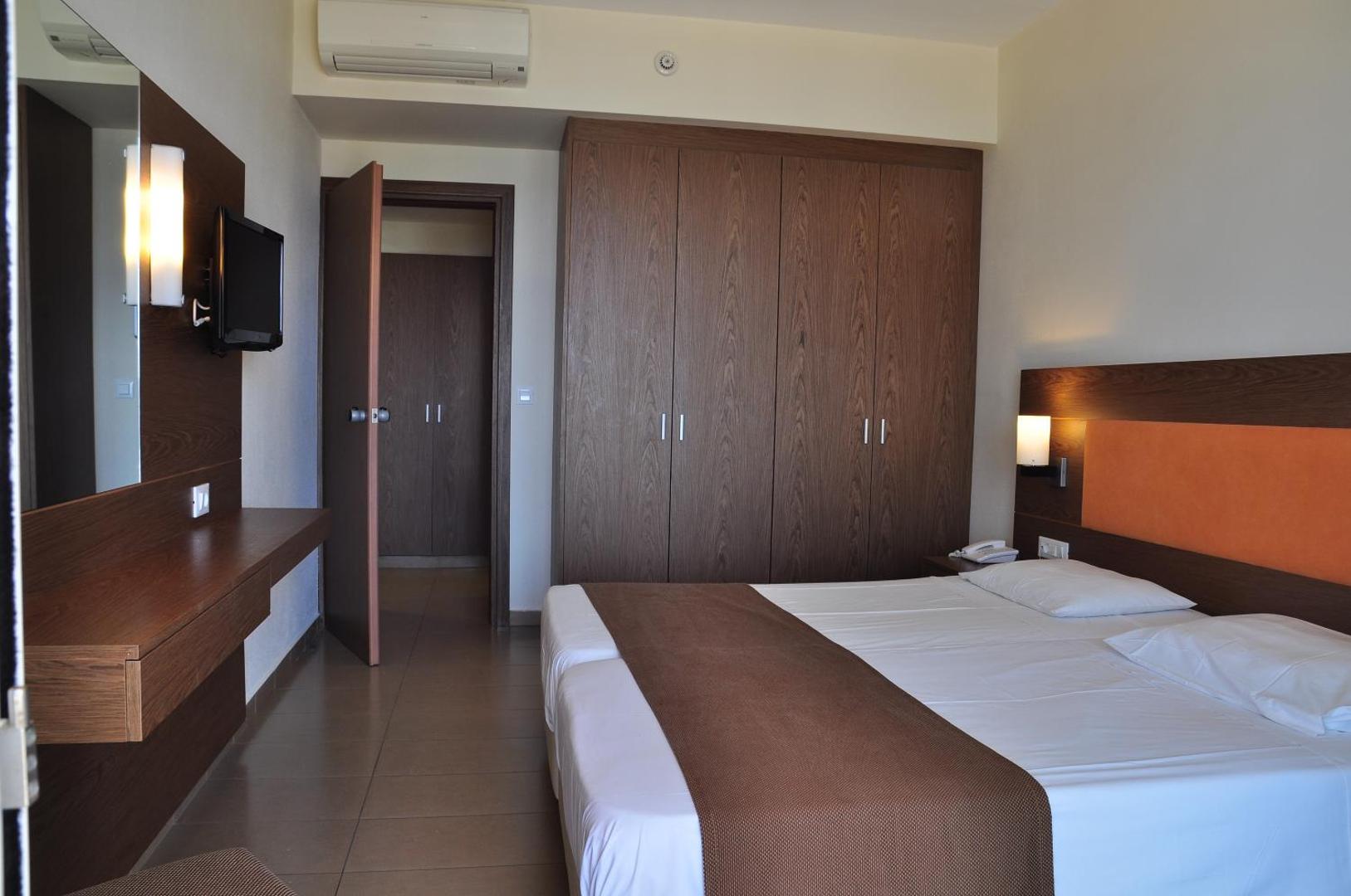 Sea Melody Beach Hotel Apartments guļamistabas interjers Rodā — koka mēbeles, iebūvētais skapis, gaisa kondicionieris un darba zona