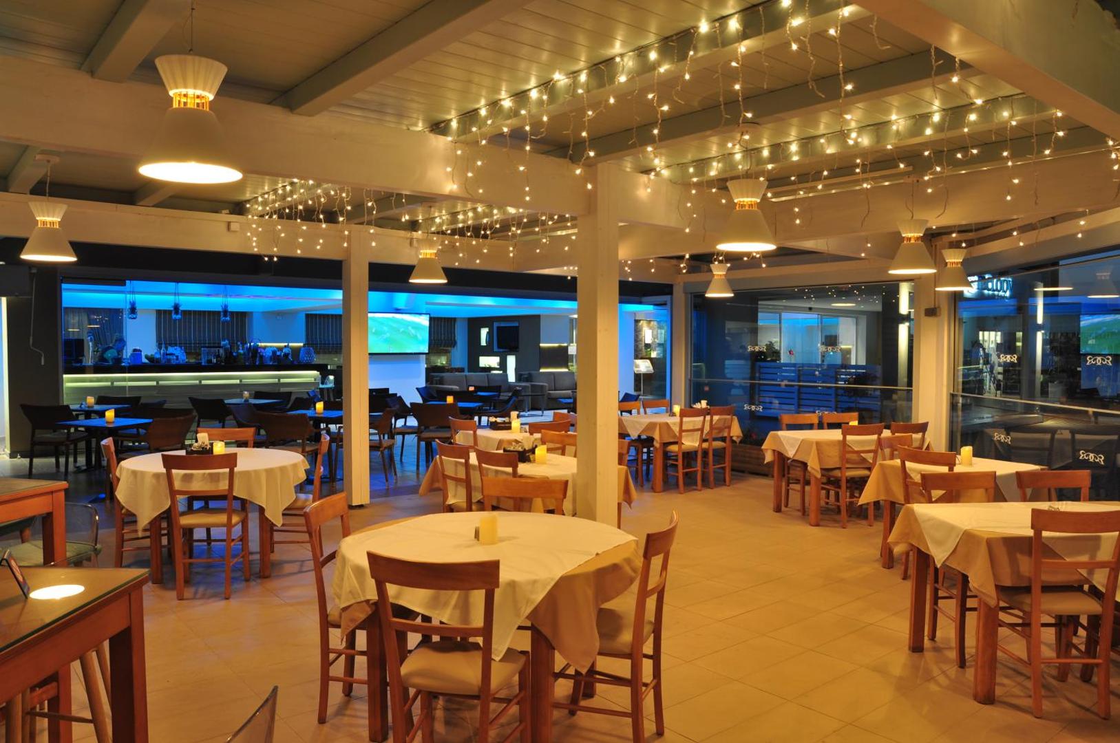 Sea Melody Beach Hotel Apartments iekštelpu restorāns ar koka galdiem, krēsliem un dekoratīvām lampiņu virtenēm mājīgai atmosfērai