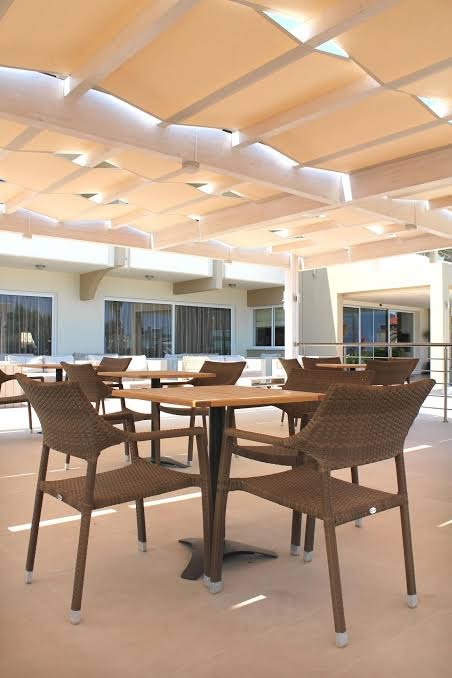 Sea Melody Beach Hotel Apartments atpūtas zona zem nojumes ar pītiem krēsliem un koka galdiem gaišos toņos