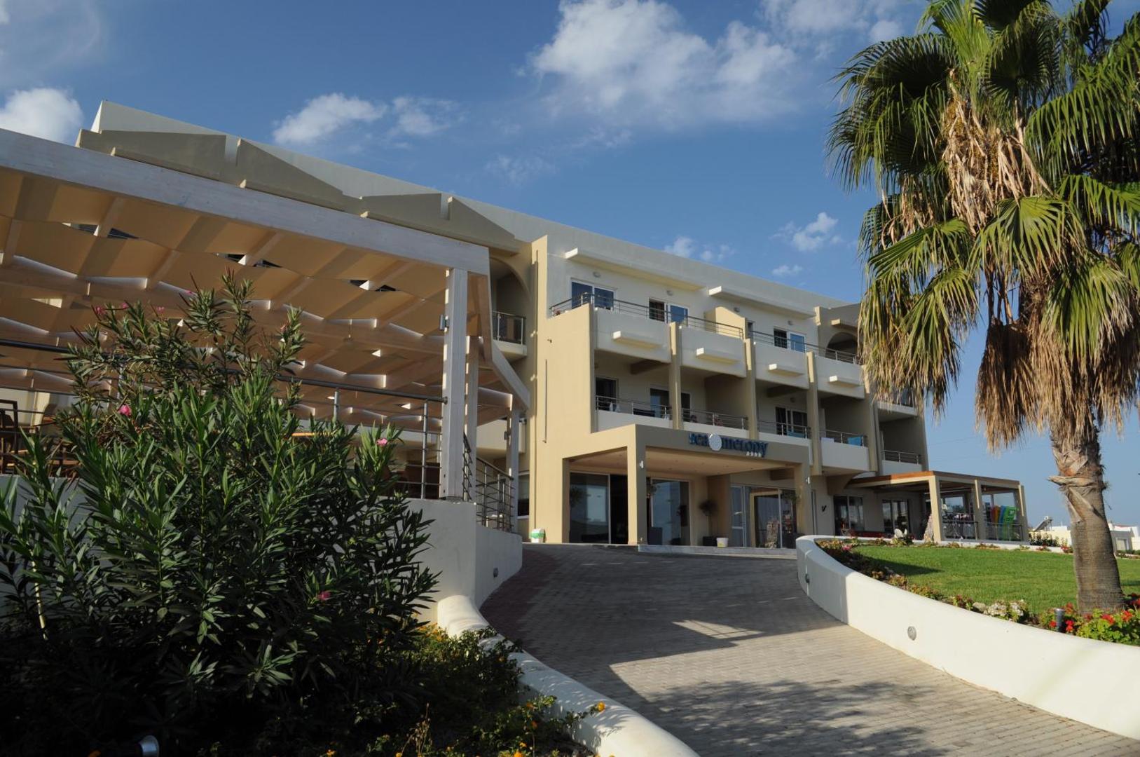 Sea Melody Beach Hotel Apartments galvenā ēka un ieeja Rodas salā — gaiša arhitektūra ar palmām un koptu zālienu