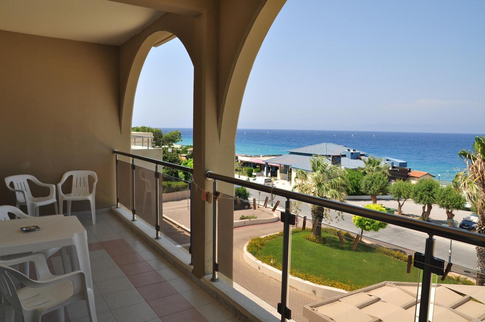 Sea Melody Beach Hotel Apartments plašais balkons ar galdu un krēsliem Rodas salā — skats uz kūrorta teritoriju un jūras piekrasti