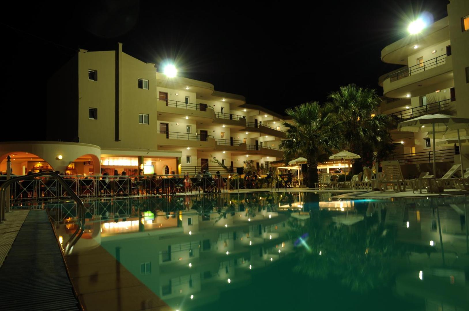 Sea Melody Beach Hotel Apartments izgaismots baseins un bārs vakarā Rodas salā — romantiska atmosfēra pie ūdens