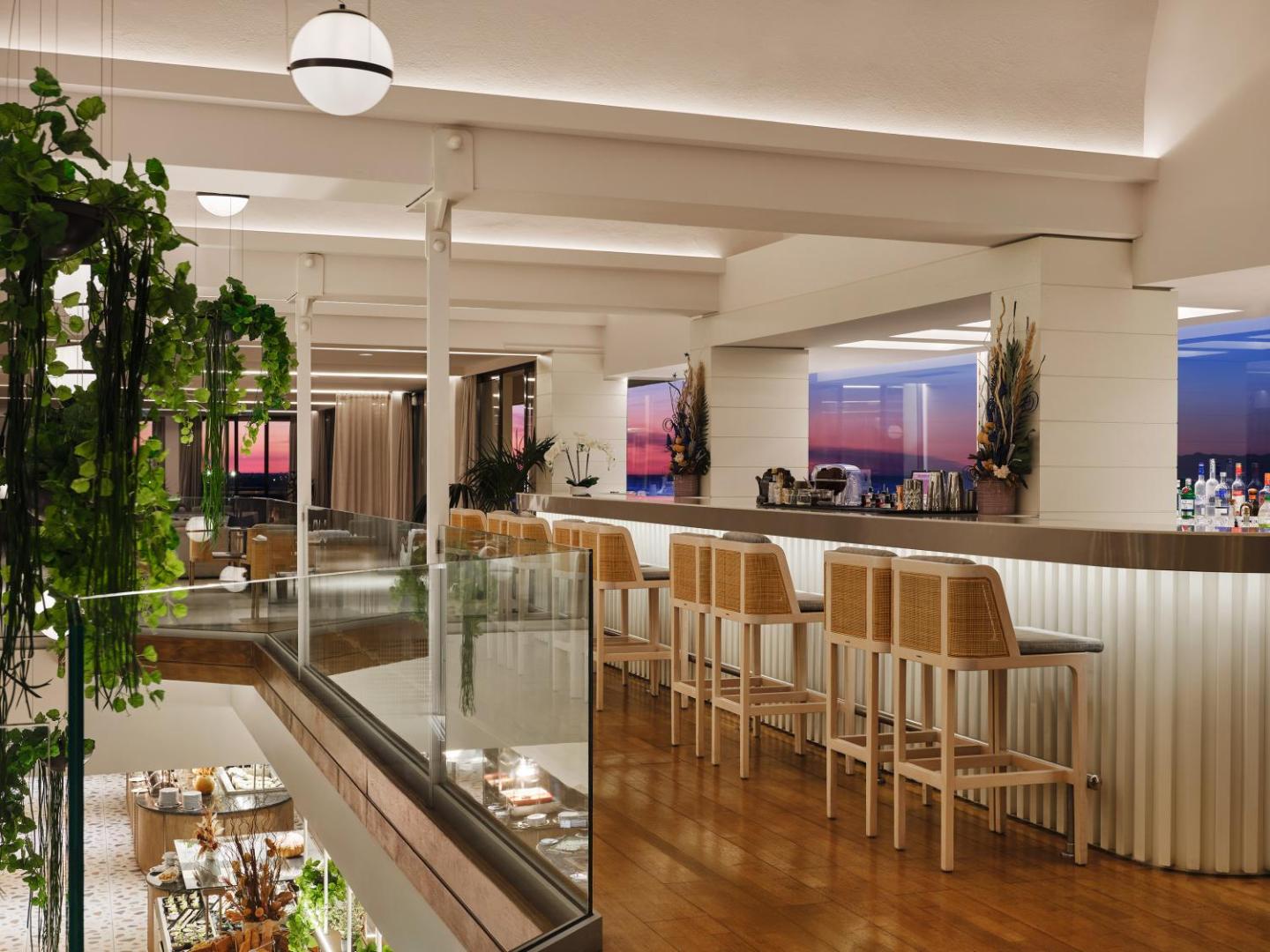 Amus Hotel & Spa bārs ar augstajiem krēsliem un skatu uz saulrietu pār Adrijas jūru Budvas piekrastē