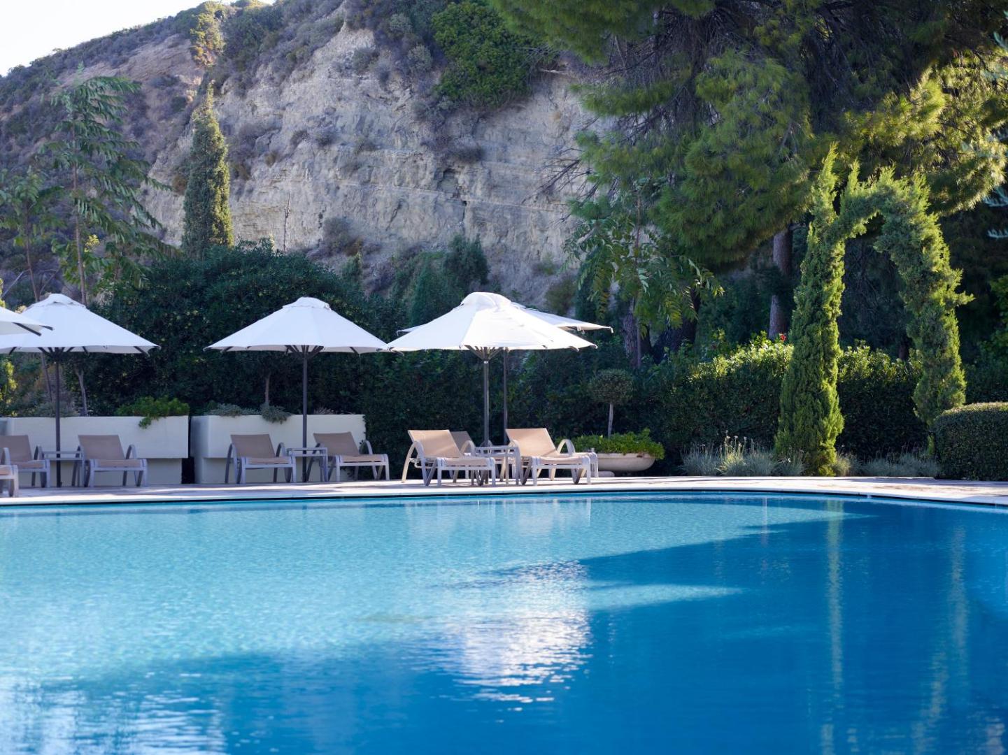 Amus Hotel & Spa baseina zona ar gaišiem saulessargiem un ērtiem zviļņiem uz kalnu un priežu meža fona.