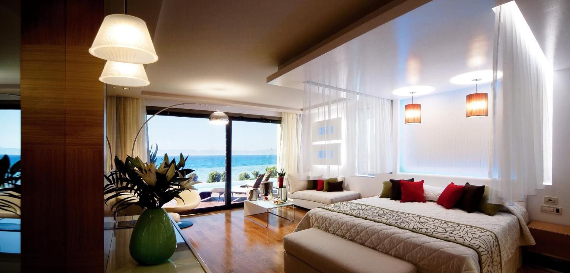 Amus Hotel & Spa luksusa numura interjers ar plašu gultu, atpūtas zonu un panorāmas logiem uz Vidusjūru